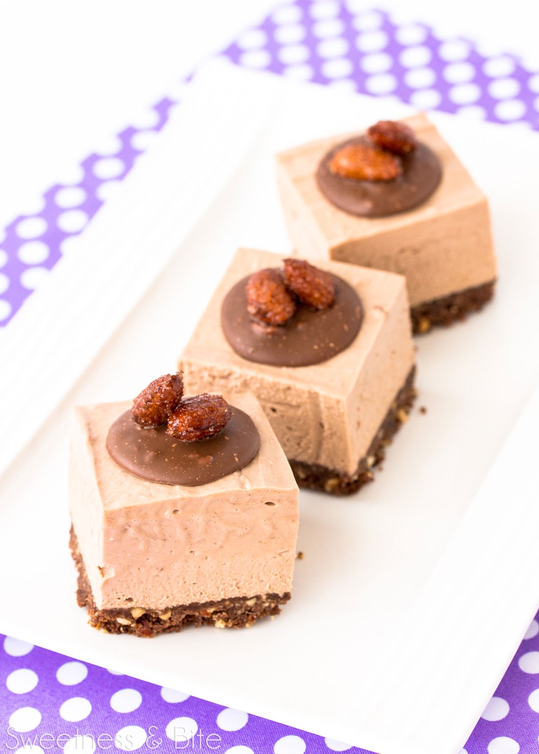 Three square pieces of cheesecake on a white rectangular plate.