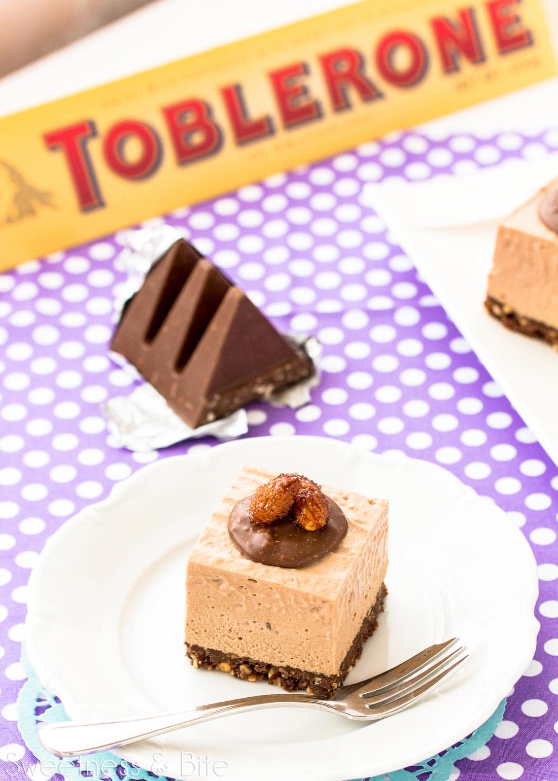 A piece of cheesecake on a white plate, with a block of Toblerone in the background.