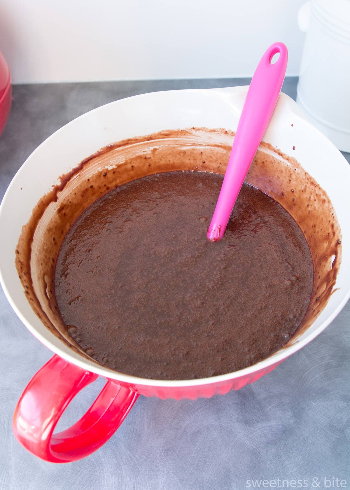 Chocolate mud cake batter in a large red bowl with a handle.