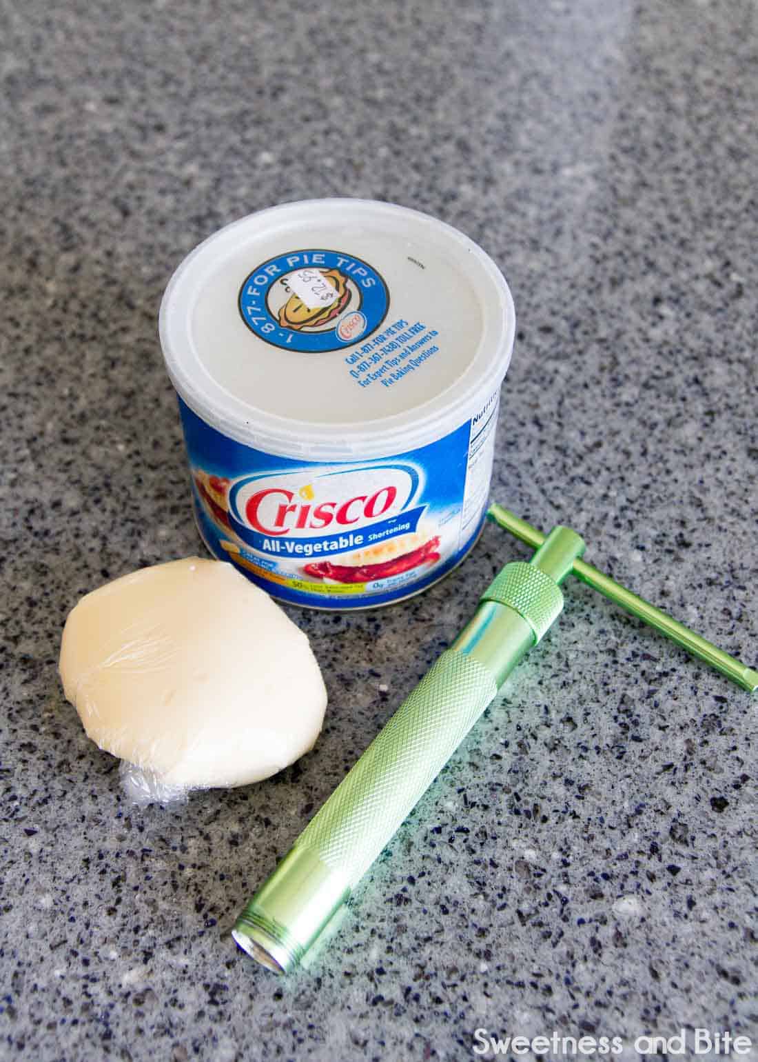 A tub of shortening, a ball of fondant and modelling chocolate and a clay extruder.