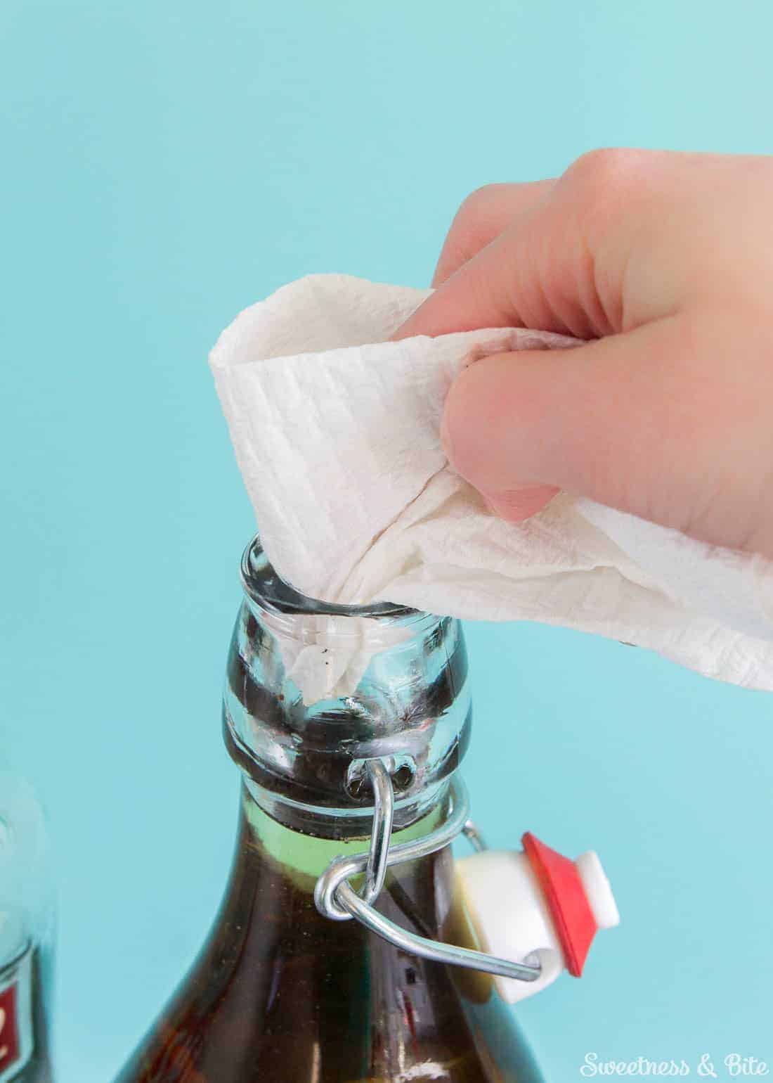 A paper towel being used to clean the top of the bottle.