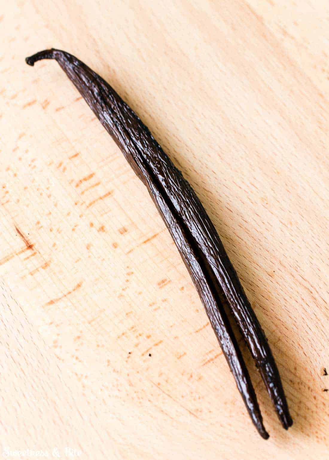 A vanilla bean that's been split up the middle, on a wooden board.