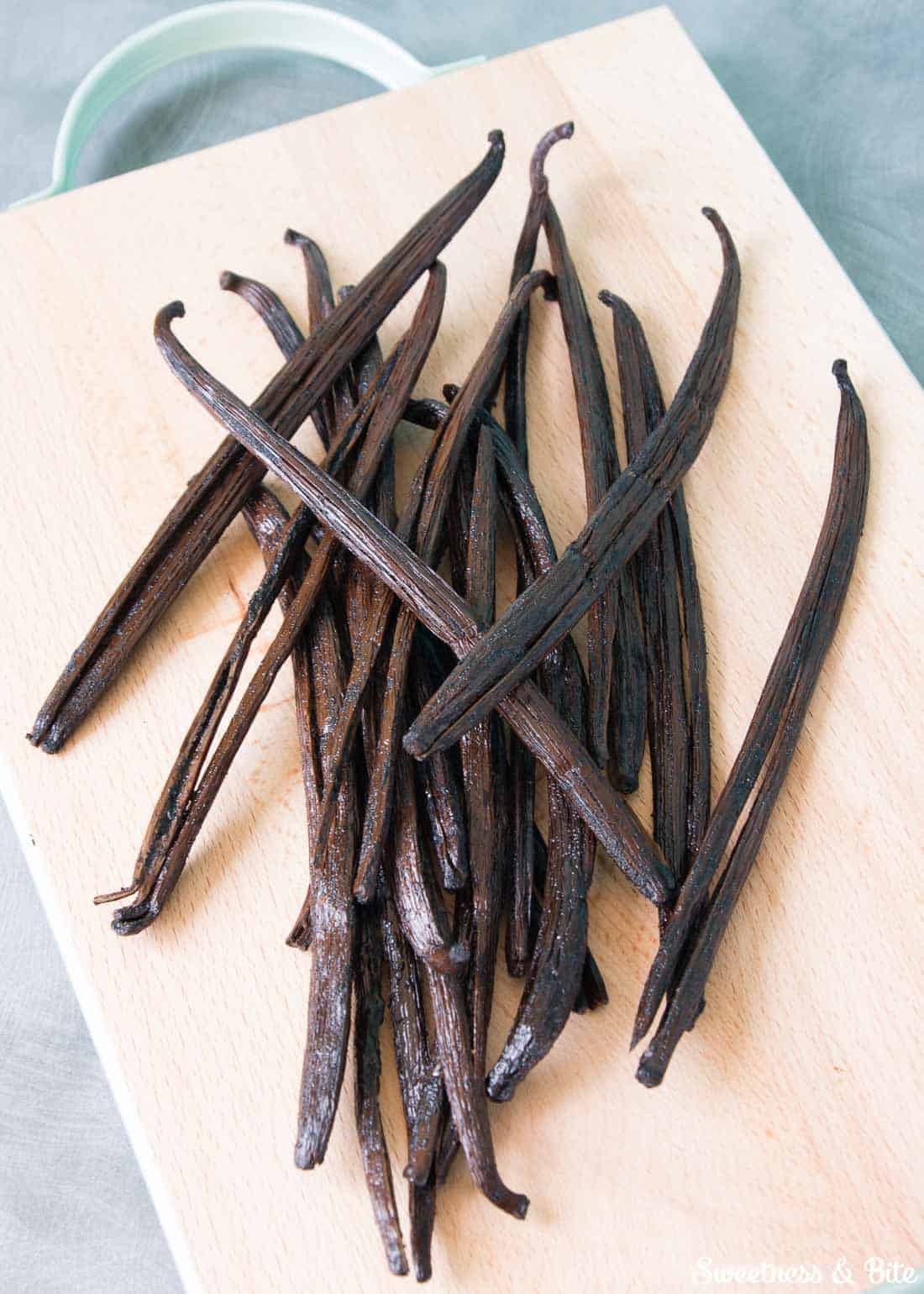 A pile of plump vanilla beans on a wooden chopping board.