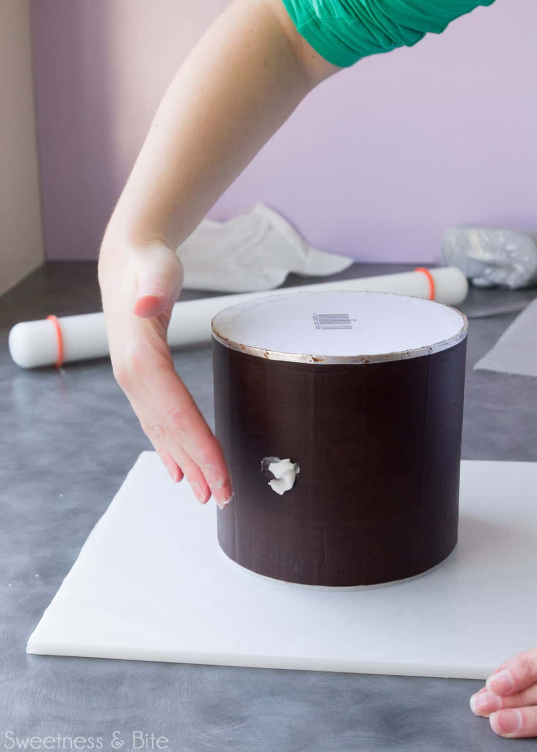 Shortening being rubbed onto the sides of a dark chocolate ganache covered cake.