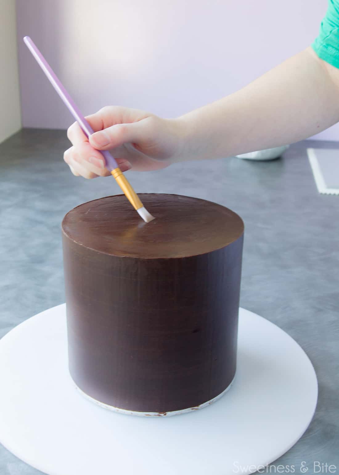 A small paintbrush being used to paint vodka onto a cake.