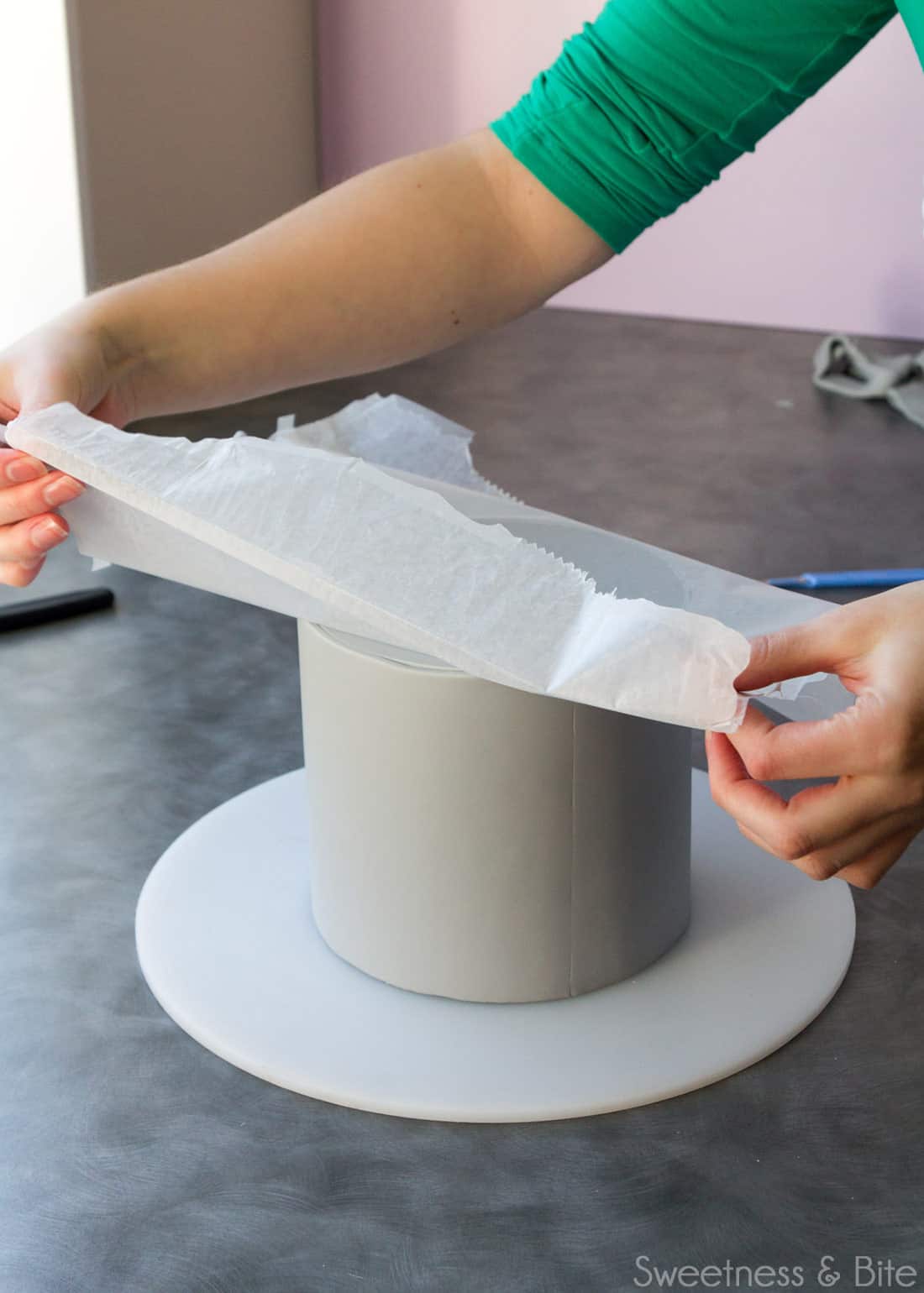 The waxed paper being peeled off the top of the cake.