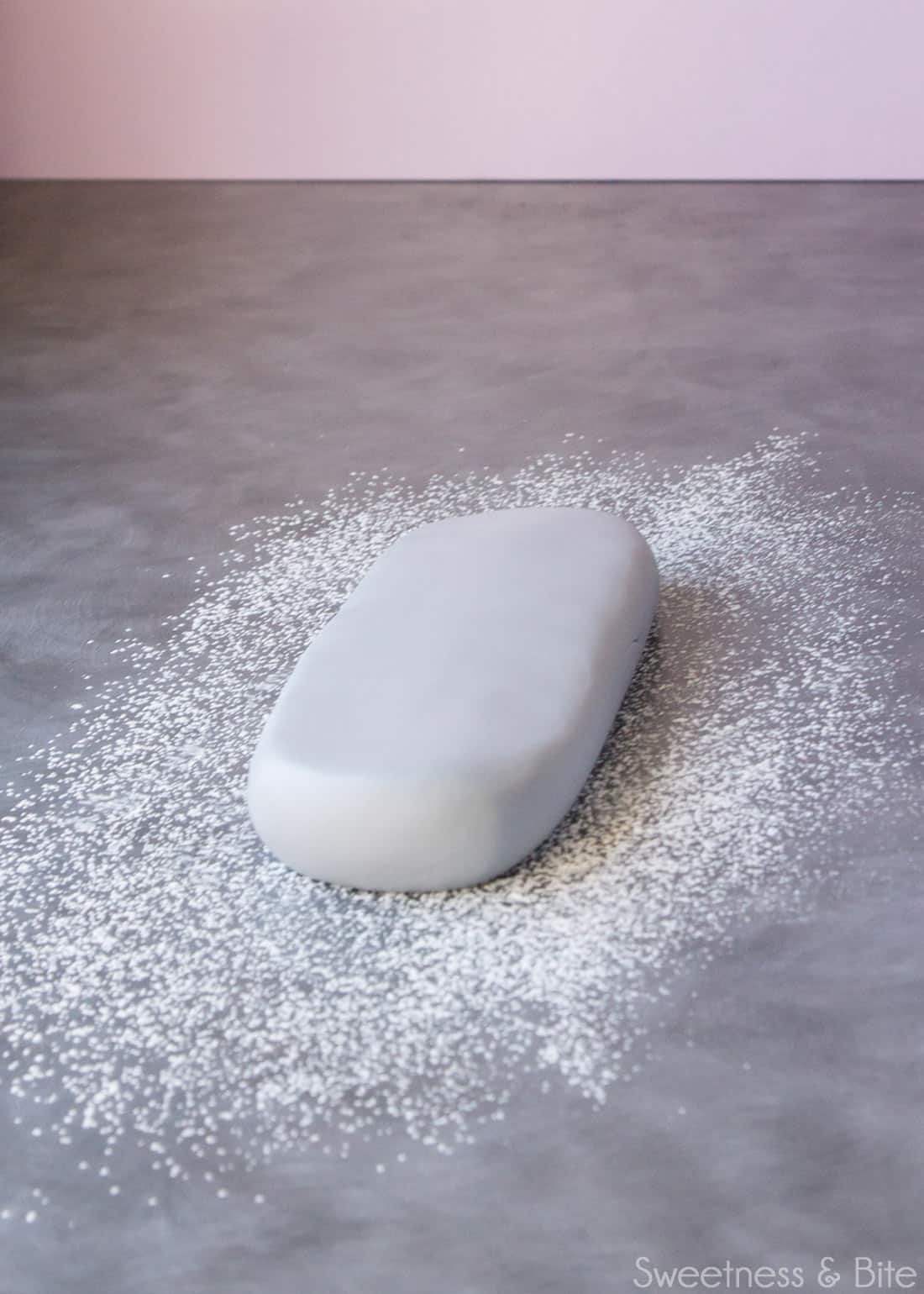A flattened sausage-shaped chunk of fondant on a cornstarch dusted bench top.