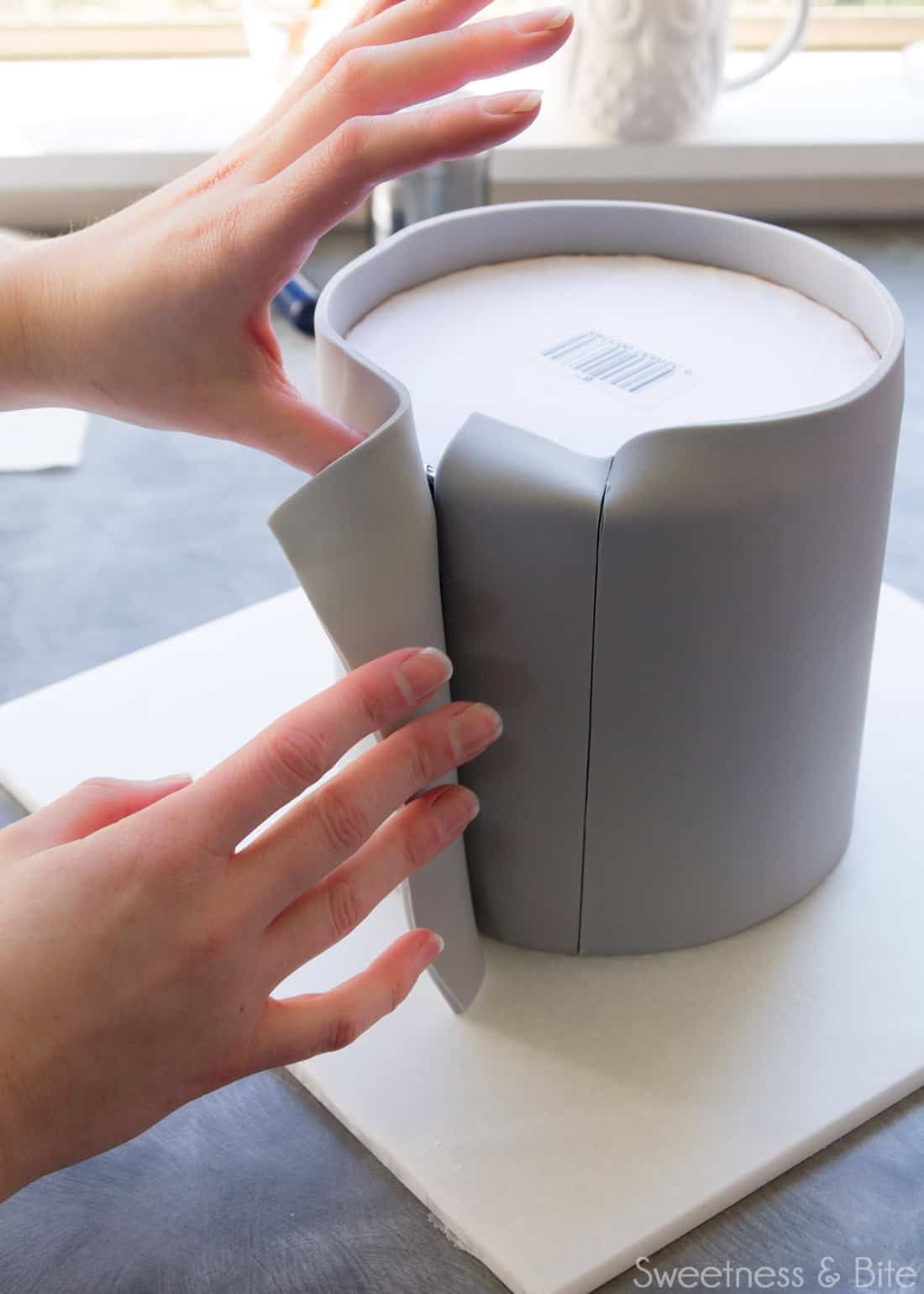 Fingers peeling back the outer edge of the fondant so the inner off-cut can be removed.