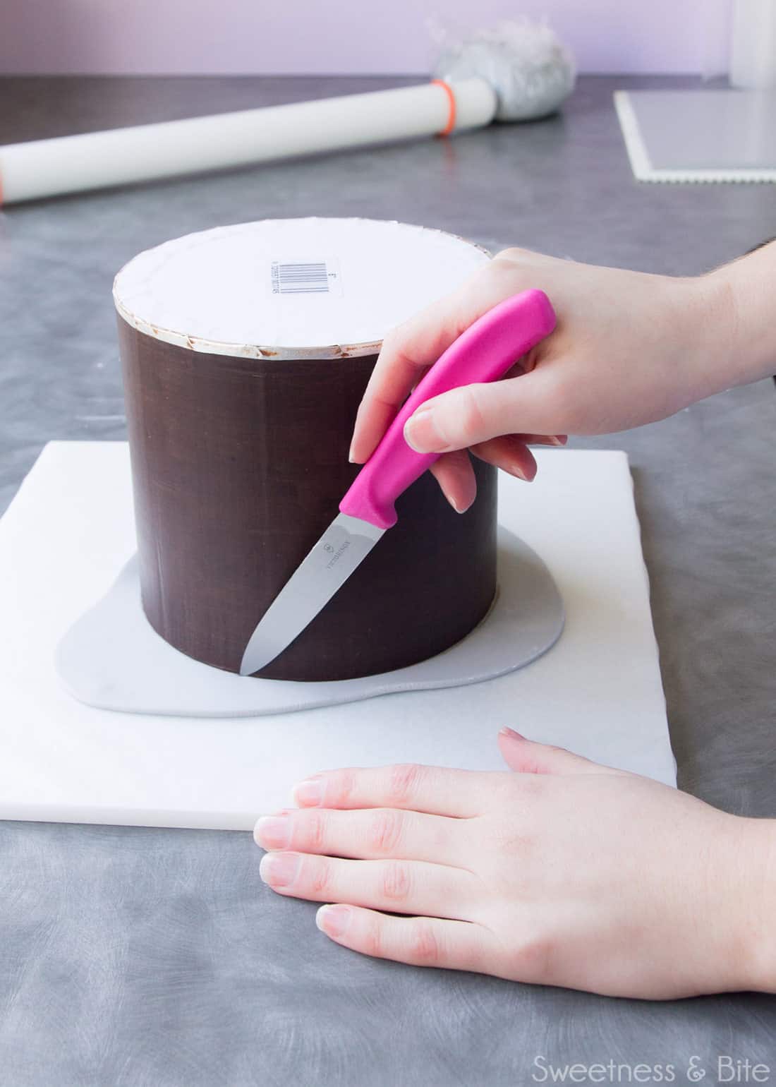 A hand using a small knife to trim the fondant on the upside down cake.