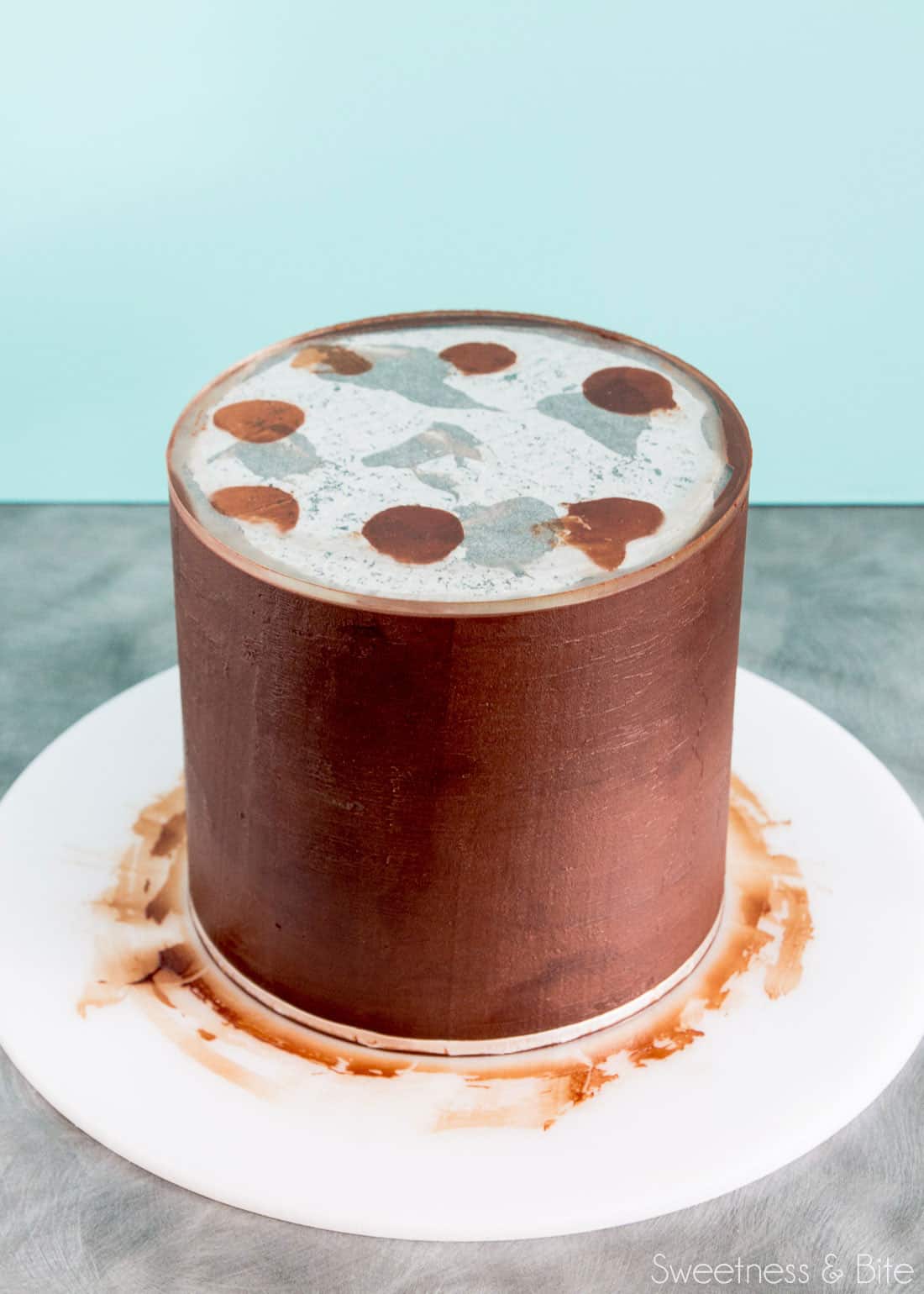 A cake being covered in ganache using an acrylic ganache board.