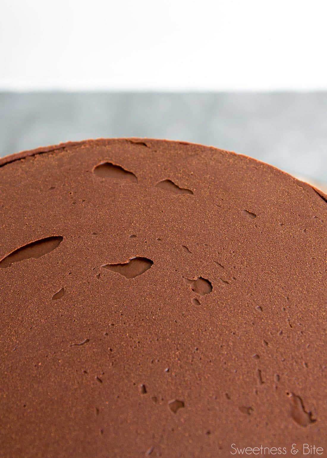 The top of a ganached cake, showing small holes from air bubbles in the ganache.