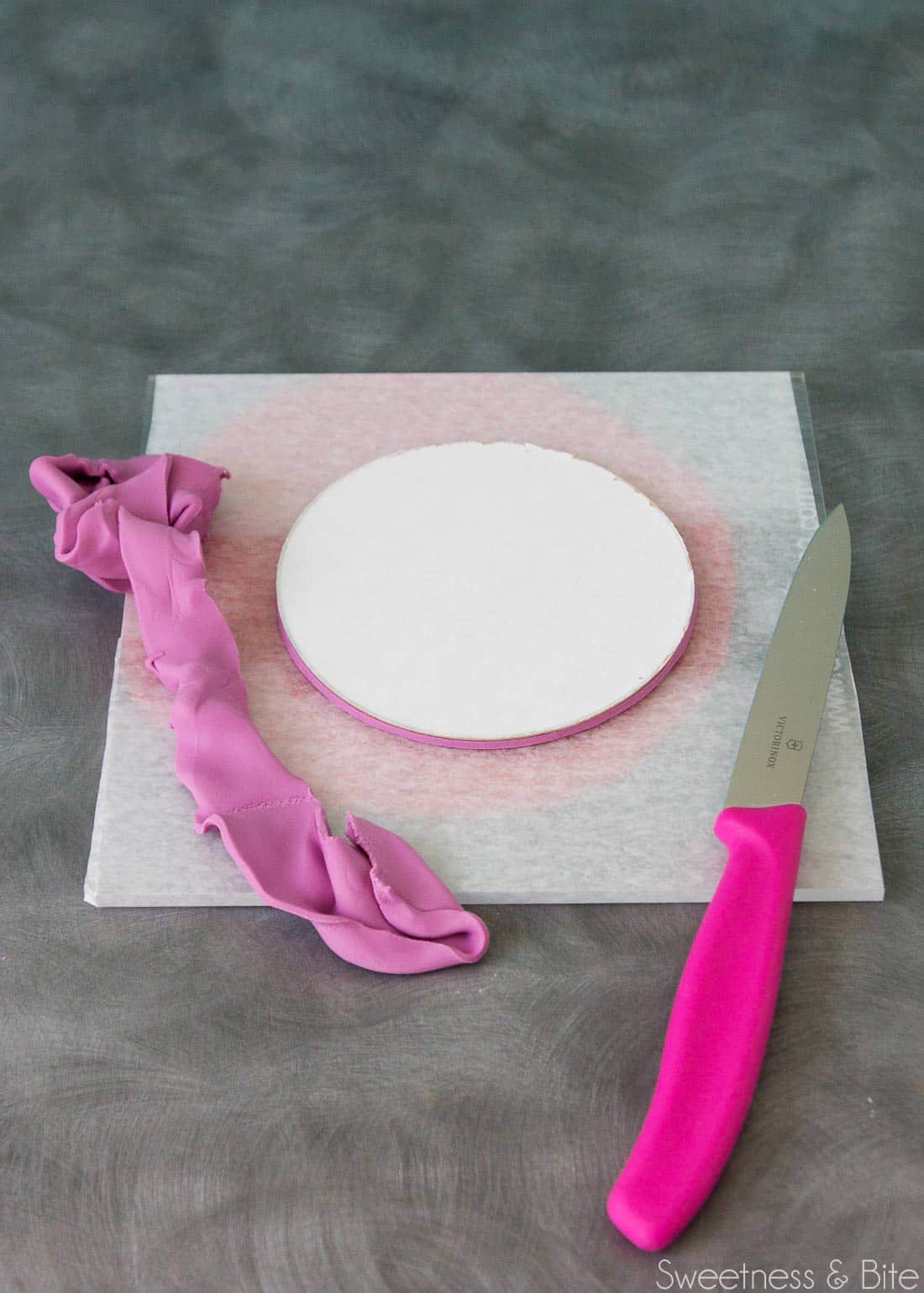 The cake card, upside down, with the fondant being trimmed by a knife.