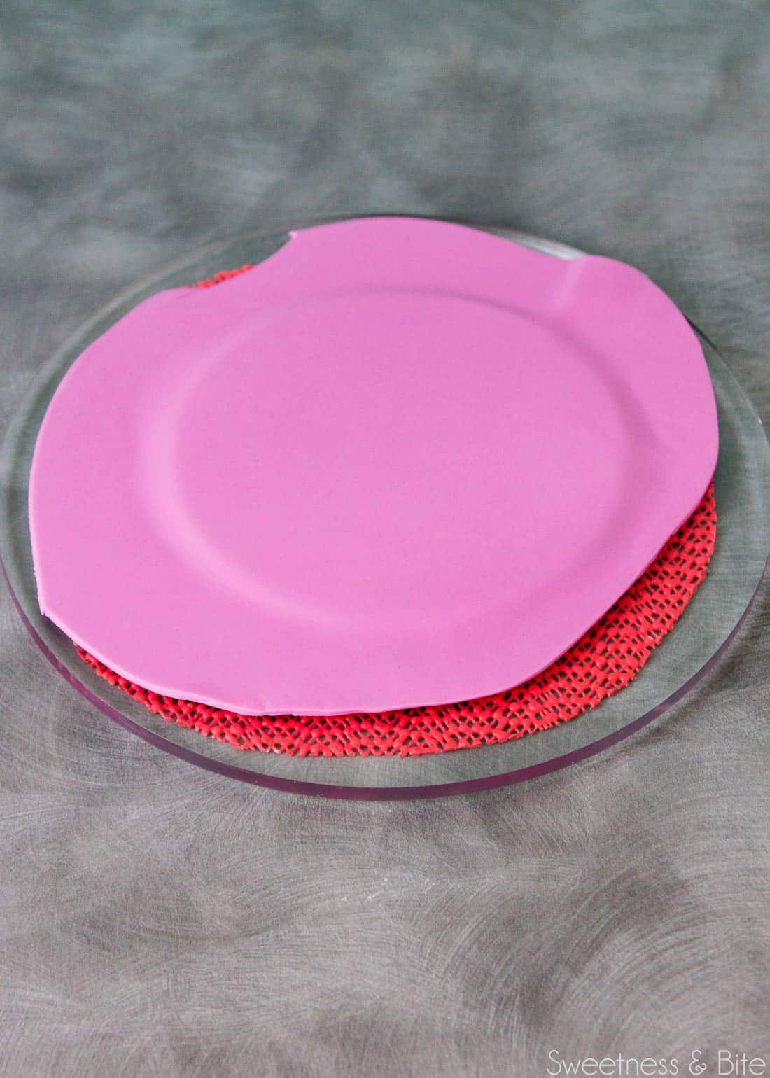 Purple fondant covering a small round cake card.