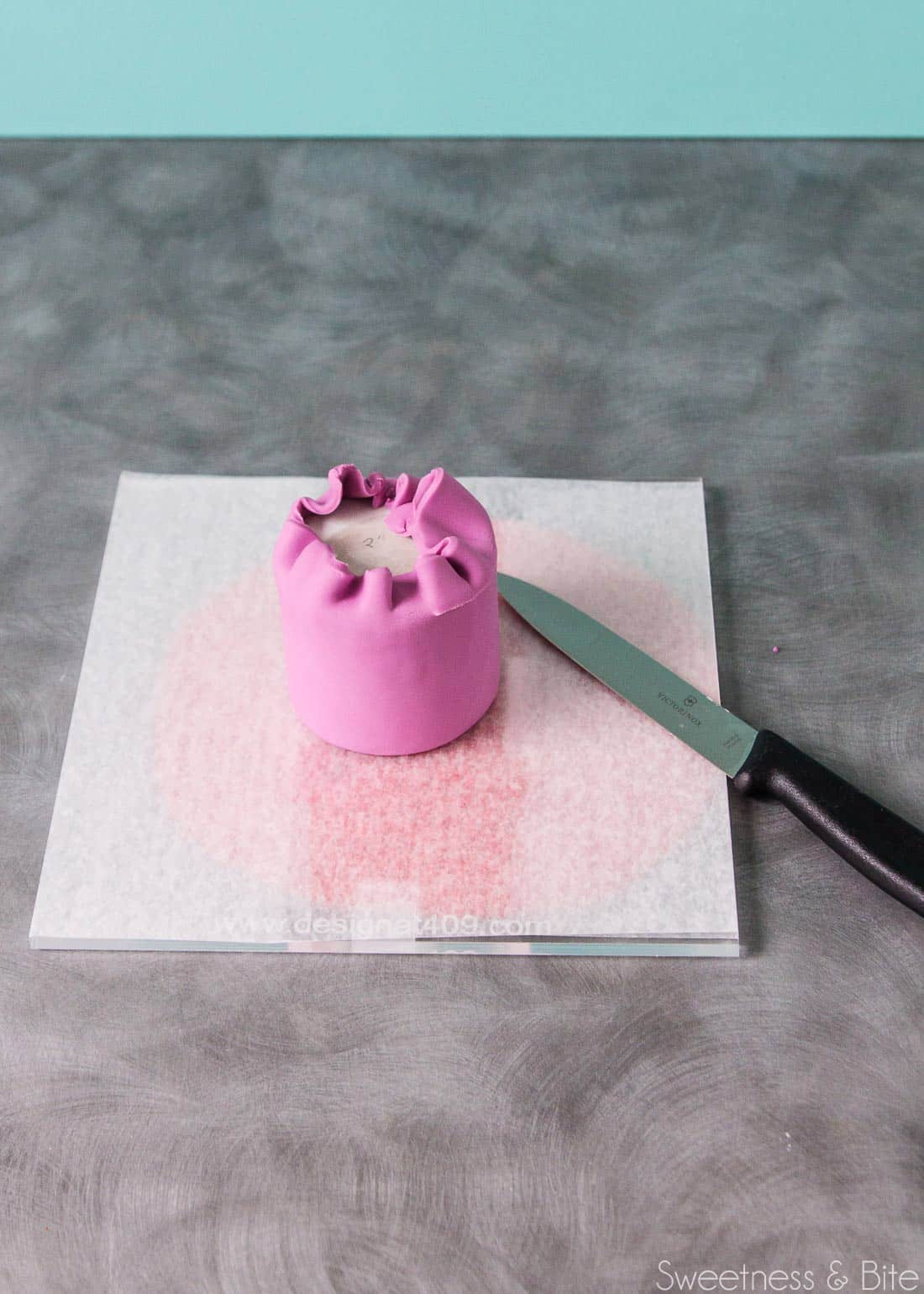 The upside down cake, with a knife trimming the edge of the fondant.