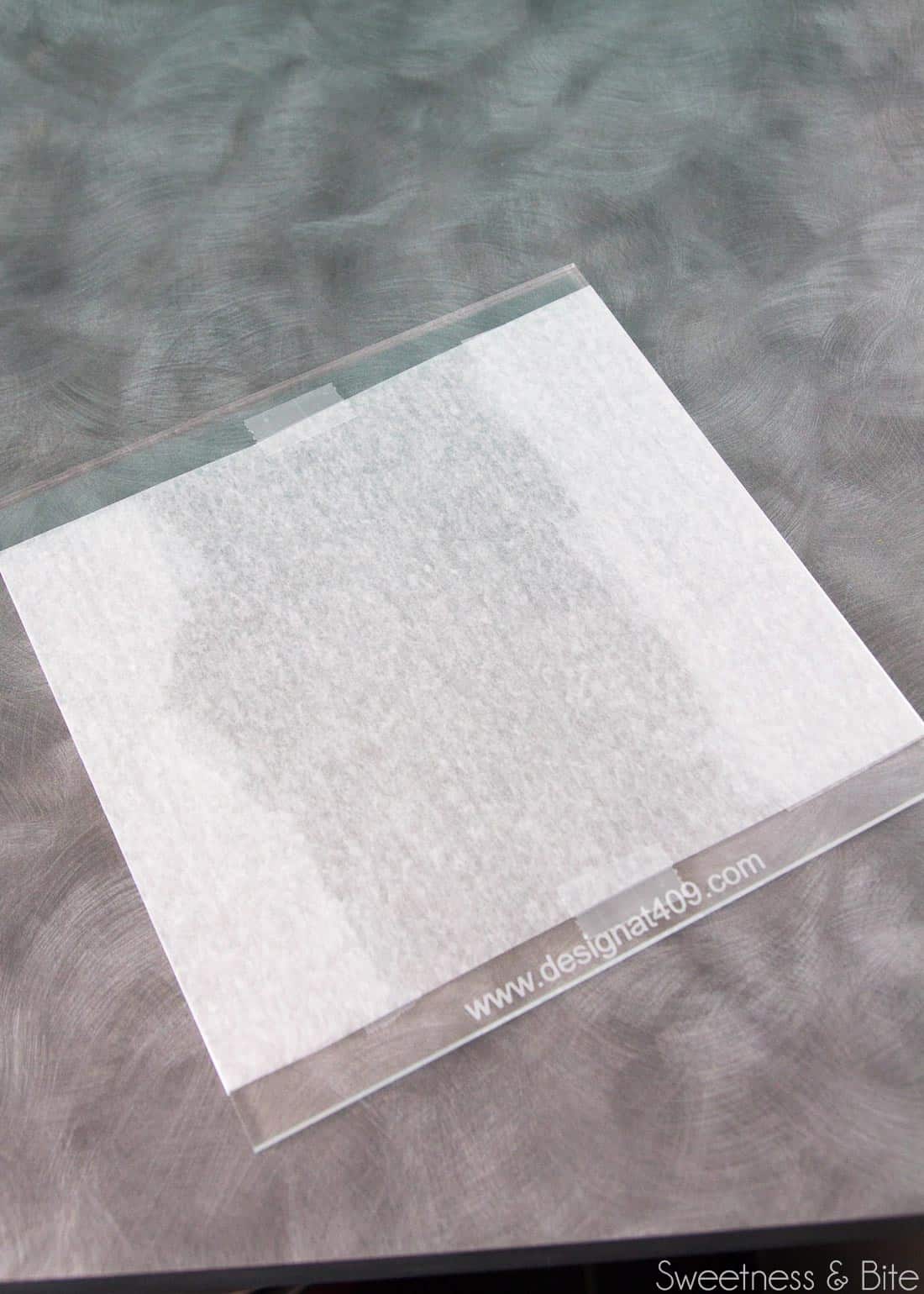 A clear acrylic cake board with a piece of waxed paper taped to it.