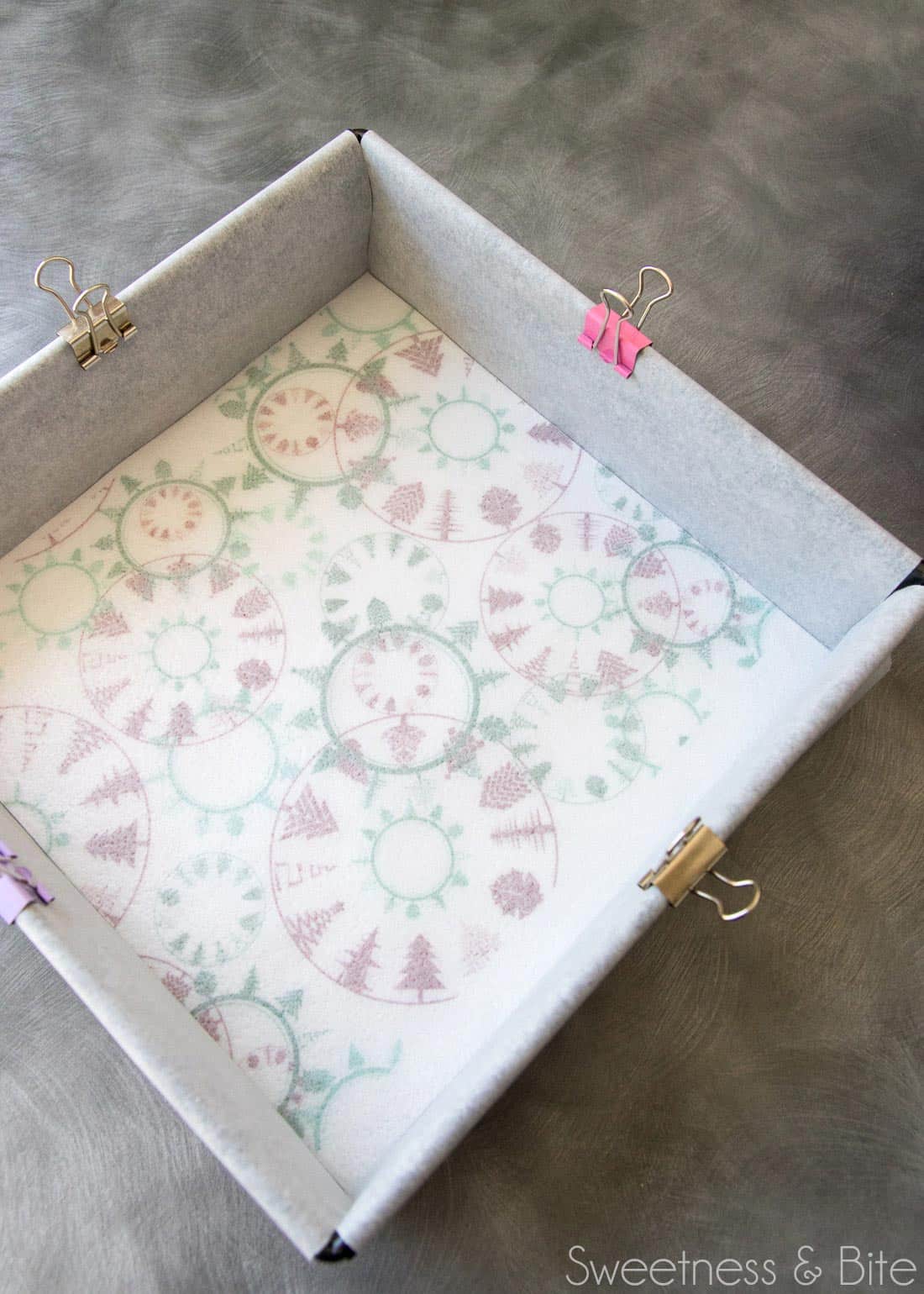 A square cake pan lined with baking paper, with a piece of printed wafter paper print-side-down in the bottom of the pan.