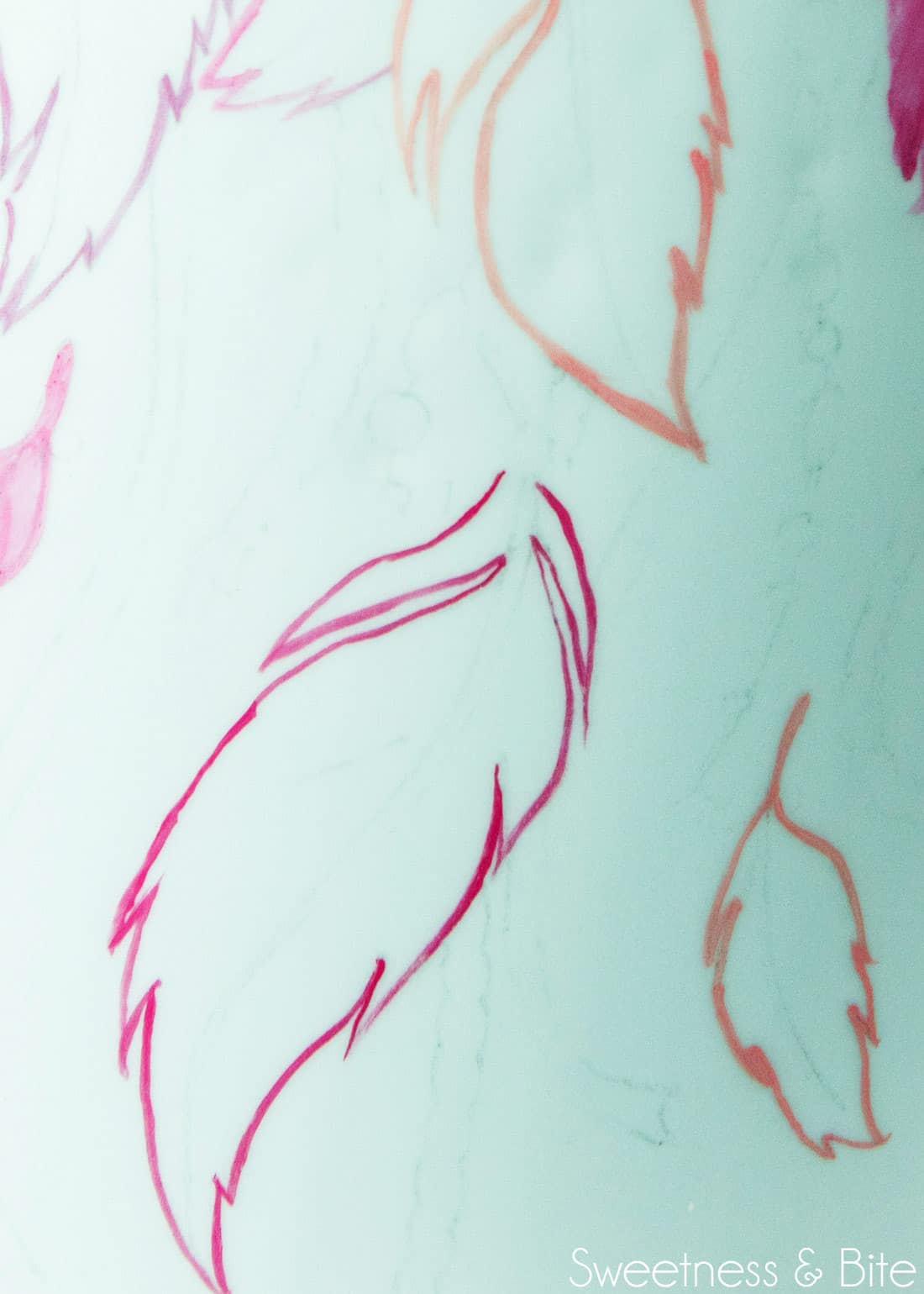 Close up of the feather design being outlined in pink edible paint.