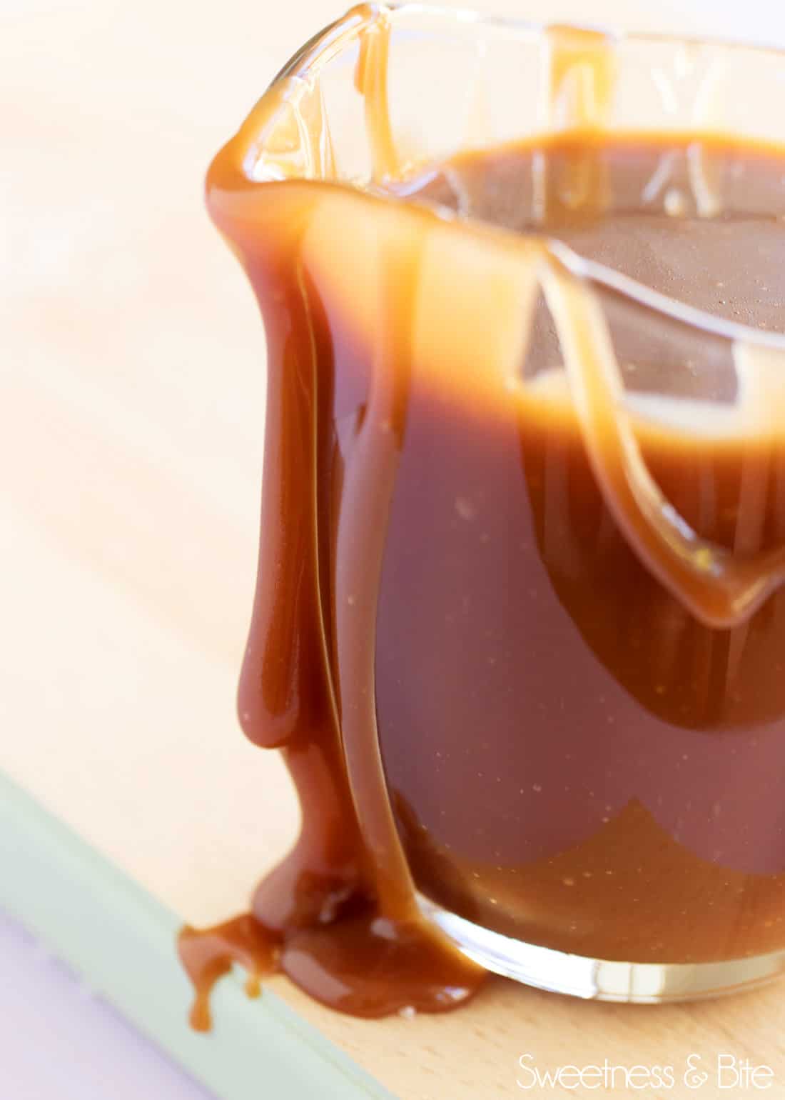 Close up of thick caramel sauce dripping down the side of a small glass jug.