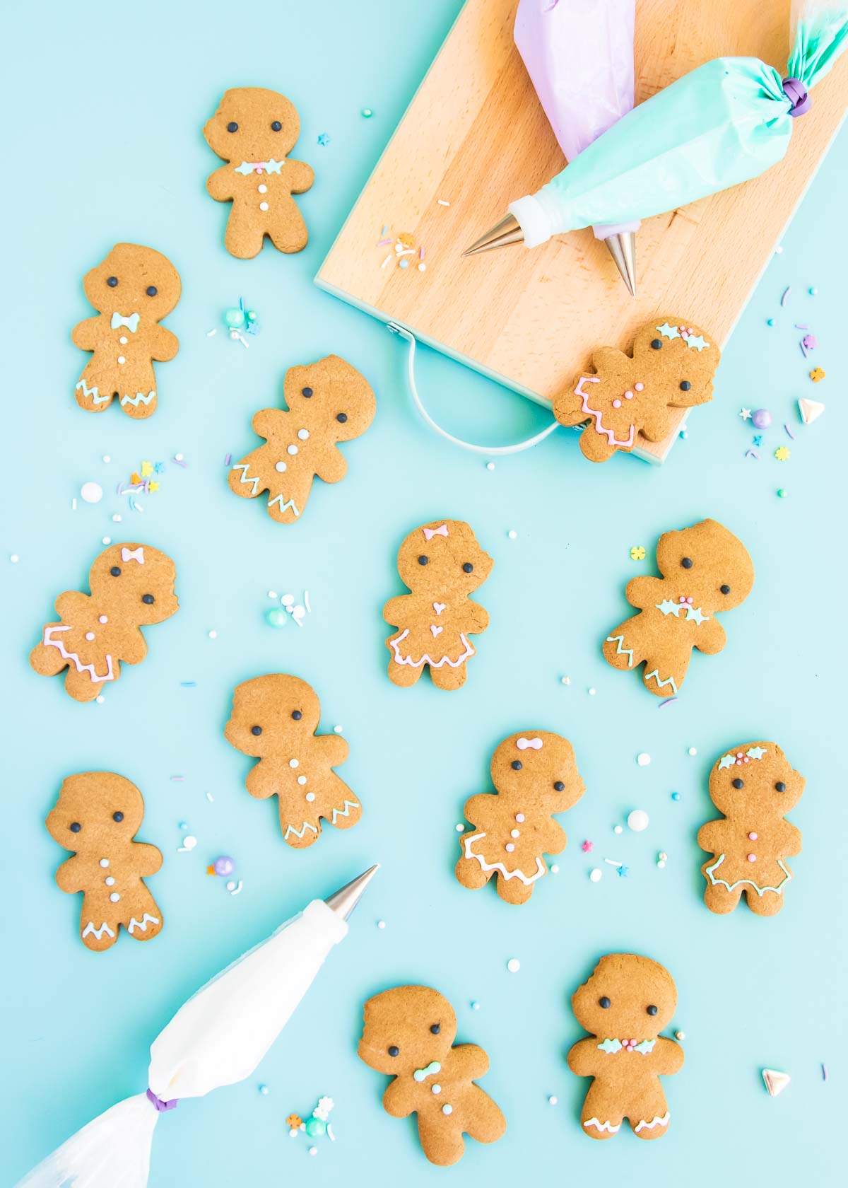 Gingerbread people cookies on a blue background, with pastel coloured royal icing in piping bags.