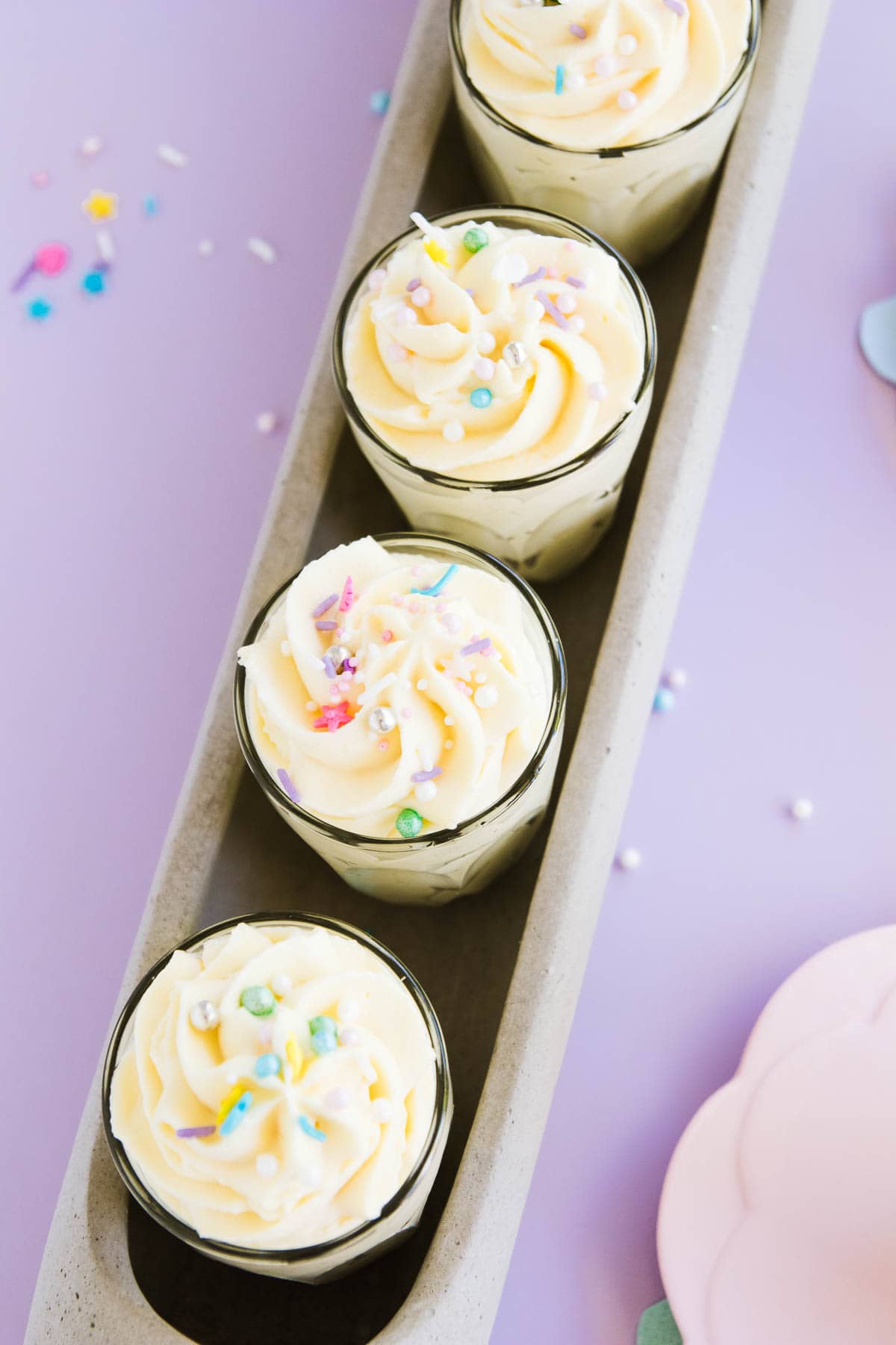Four small glasses of white chocolate mousse, sprinkled with pastel sprinkles.