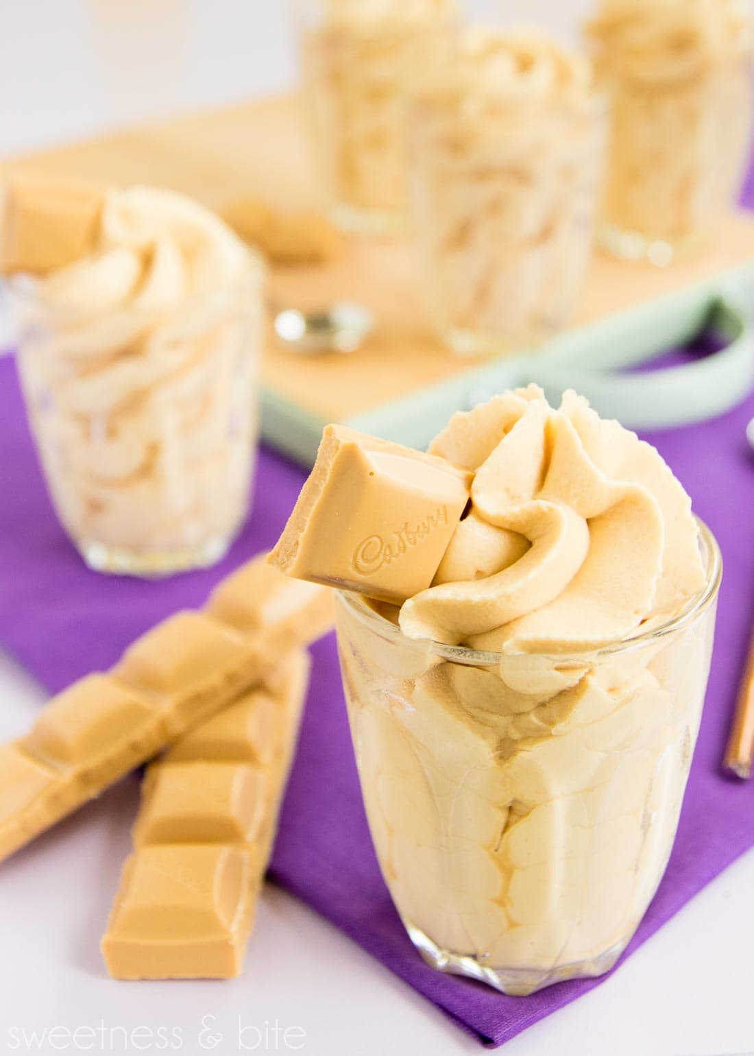 Caramilk mousse piped into a small glass with a square of Caramilk chocolate on top and two rows of chocolate in the background.