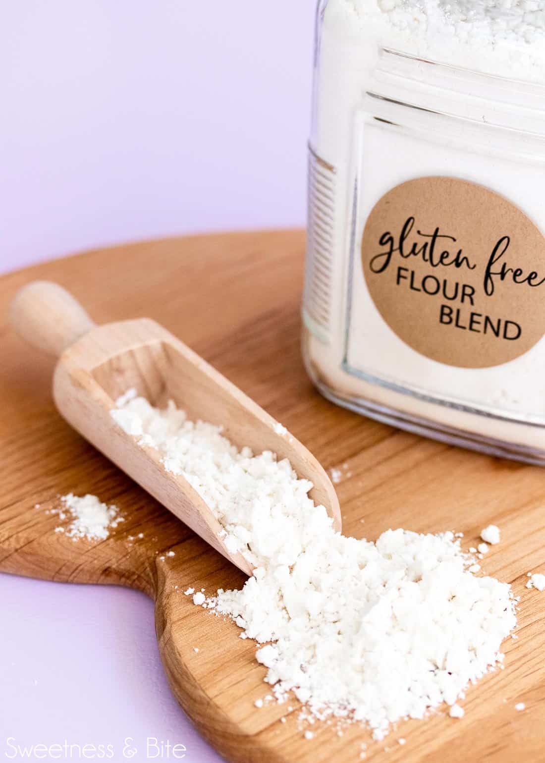 Jar of gluten free flour and a scoop of flour on a wooden board.