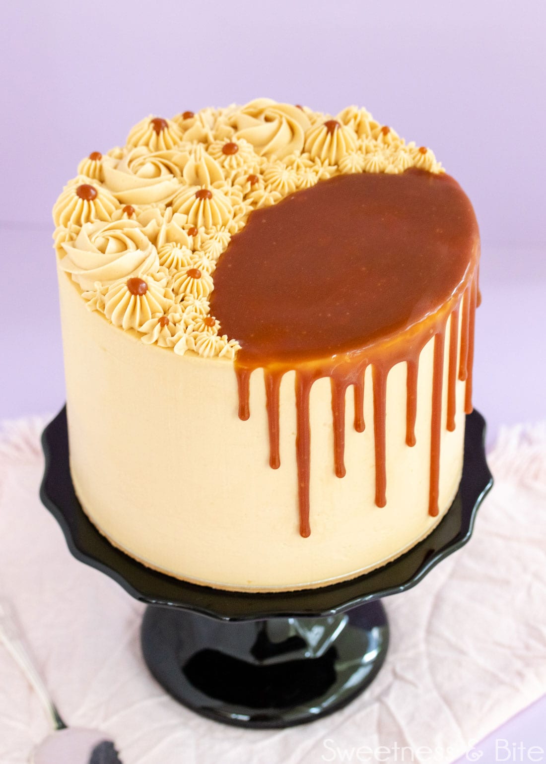 Caramel mud cake on a black cake stand, decorated with swirls of caramel buttercream on top, and a caramel sauce drip. 