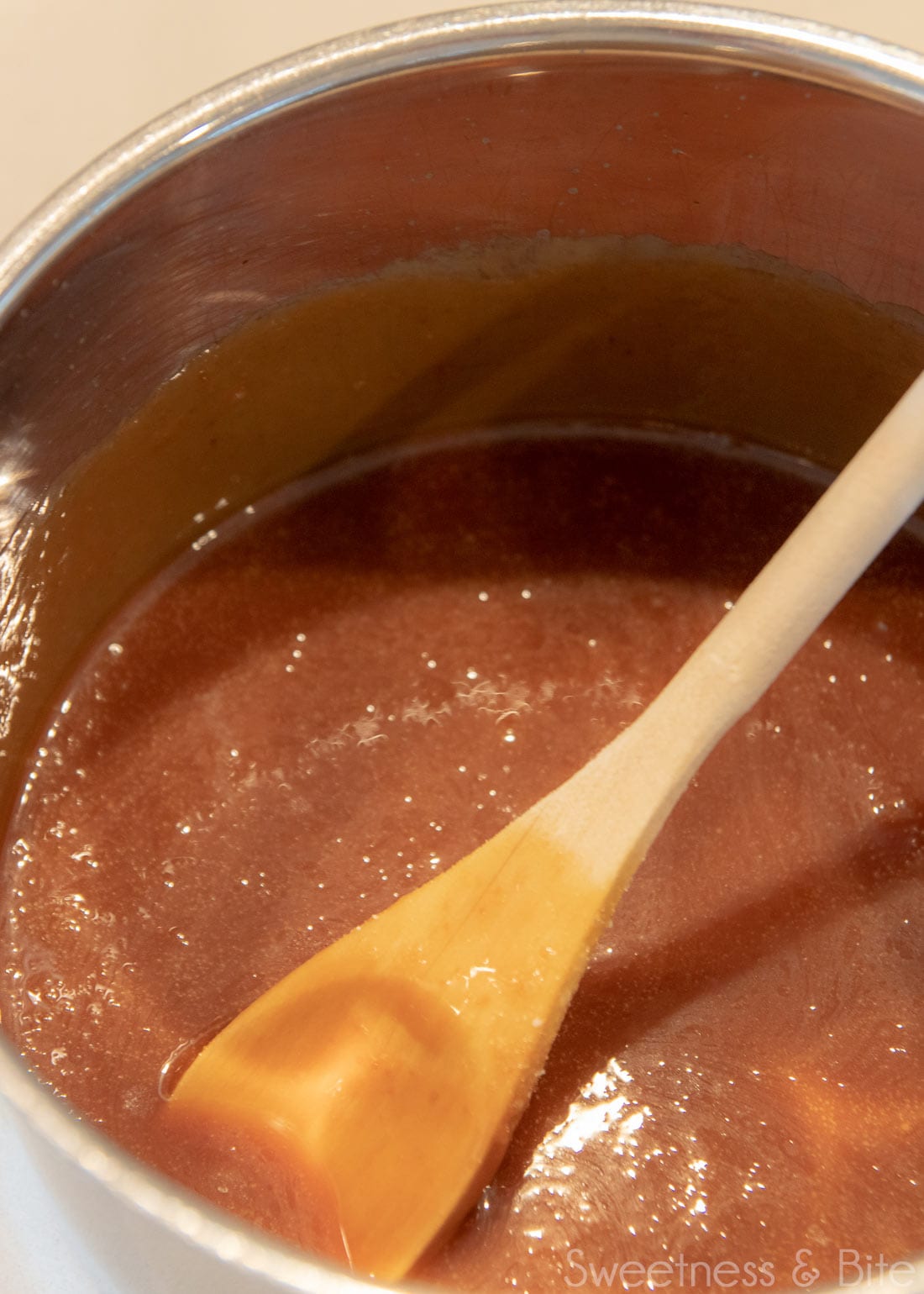 A saucepan with caramel sauce in it, with a wooden spoon.