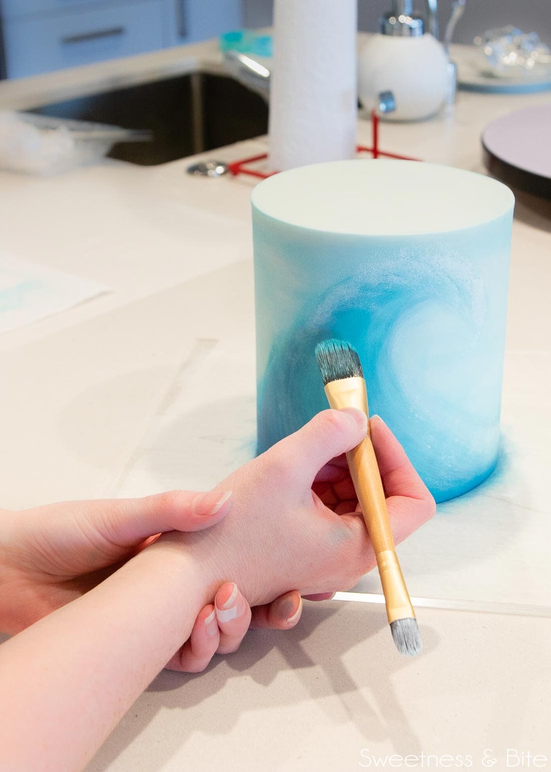 Painting a wave on the front of a blue cake.