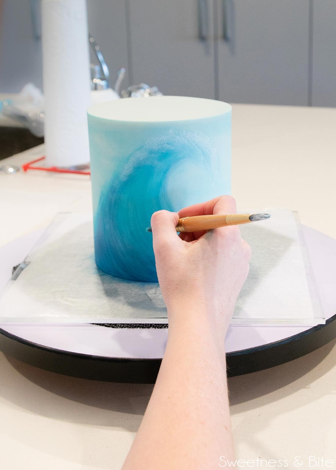 Painting a wave on a blue cake, wrist resting on the edge of a turntable.