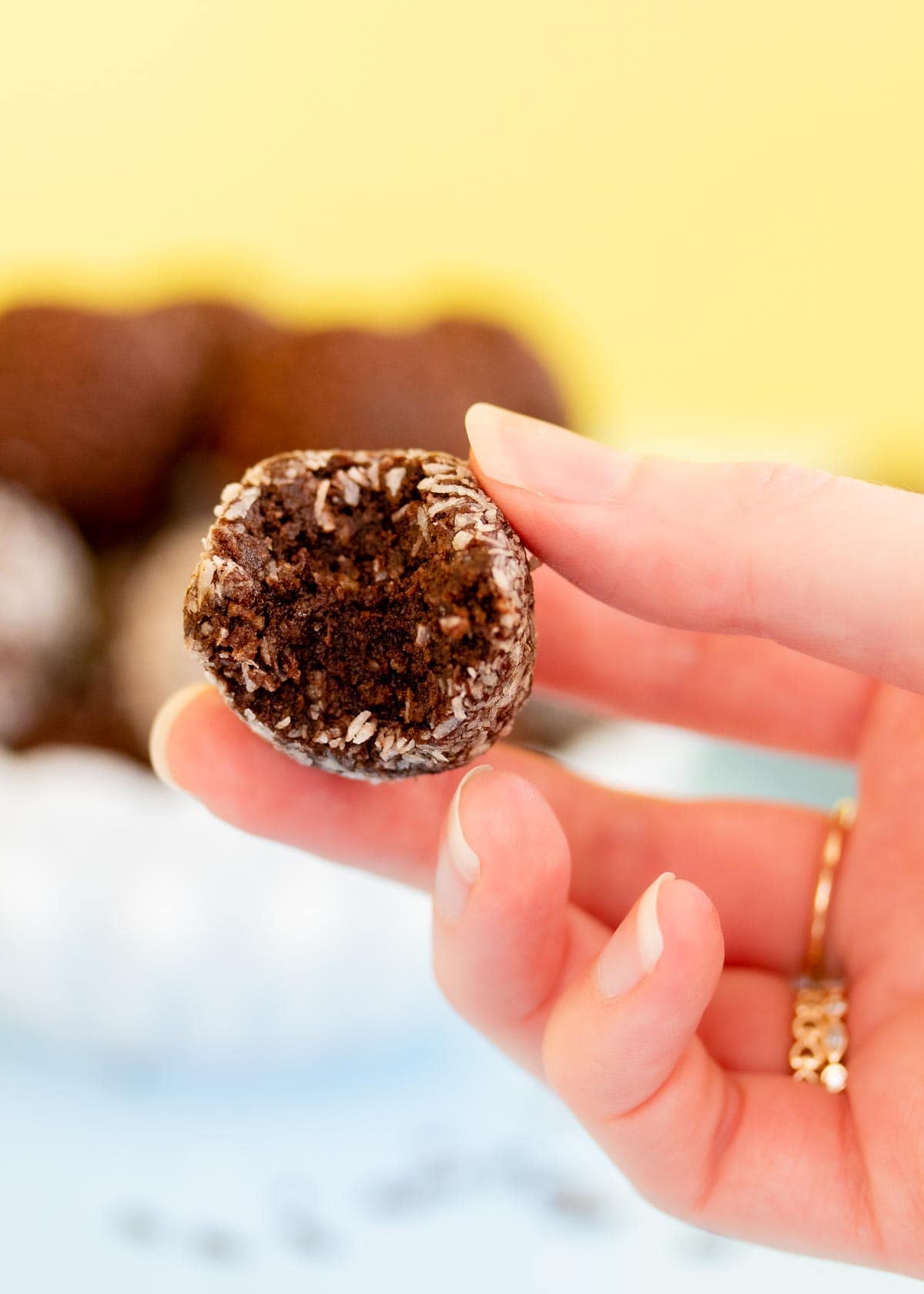 A hand holding a truffle that has had a bite taken out of it.