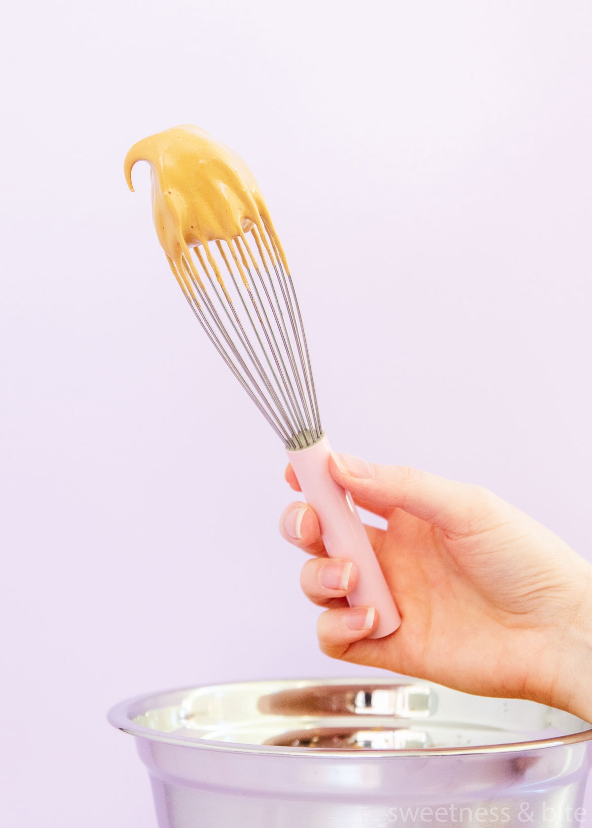 A hand holding a pink handled whisk with a dollop of whipped coffee on it.