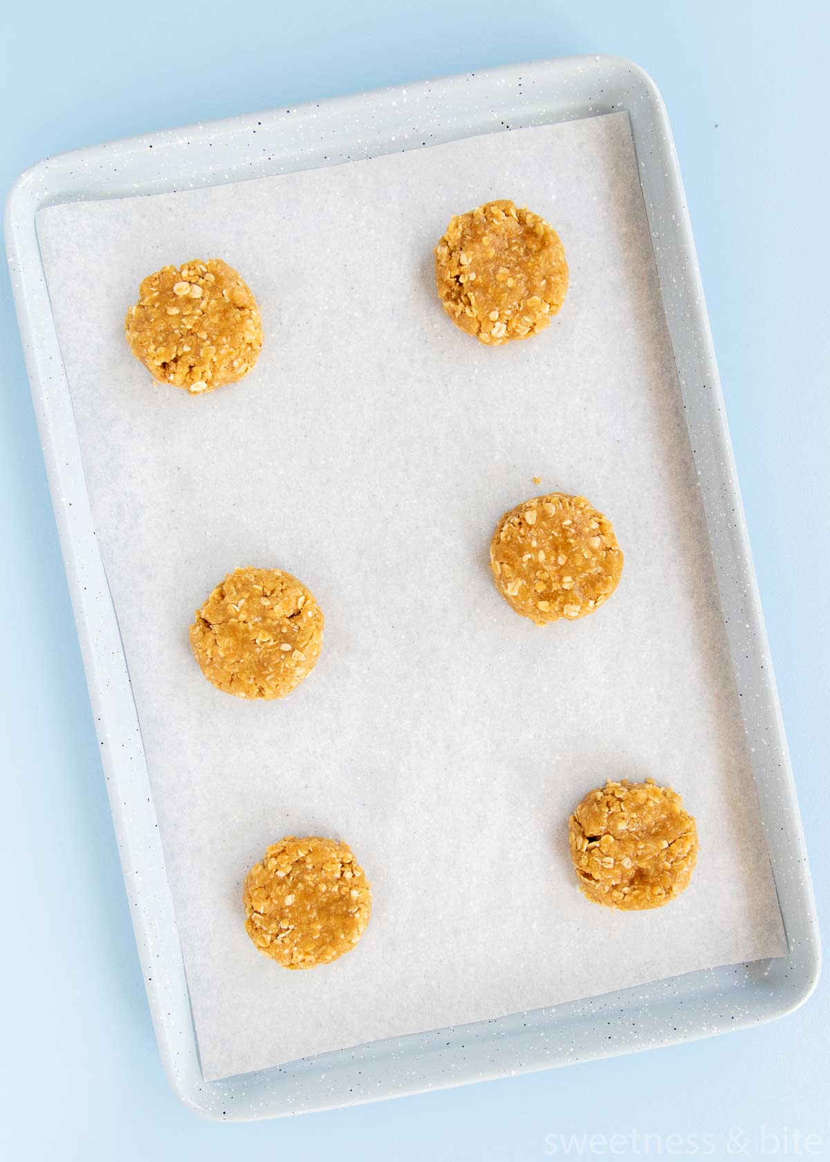 Six Anzac biscuit dough balls on a tray.