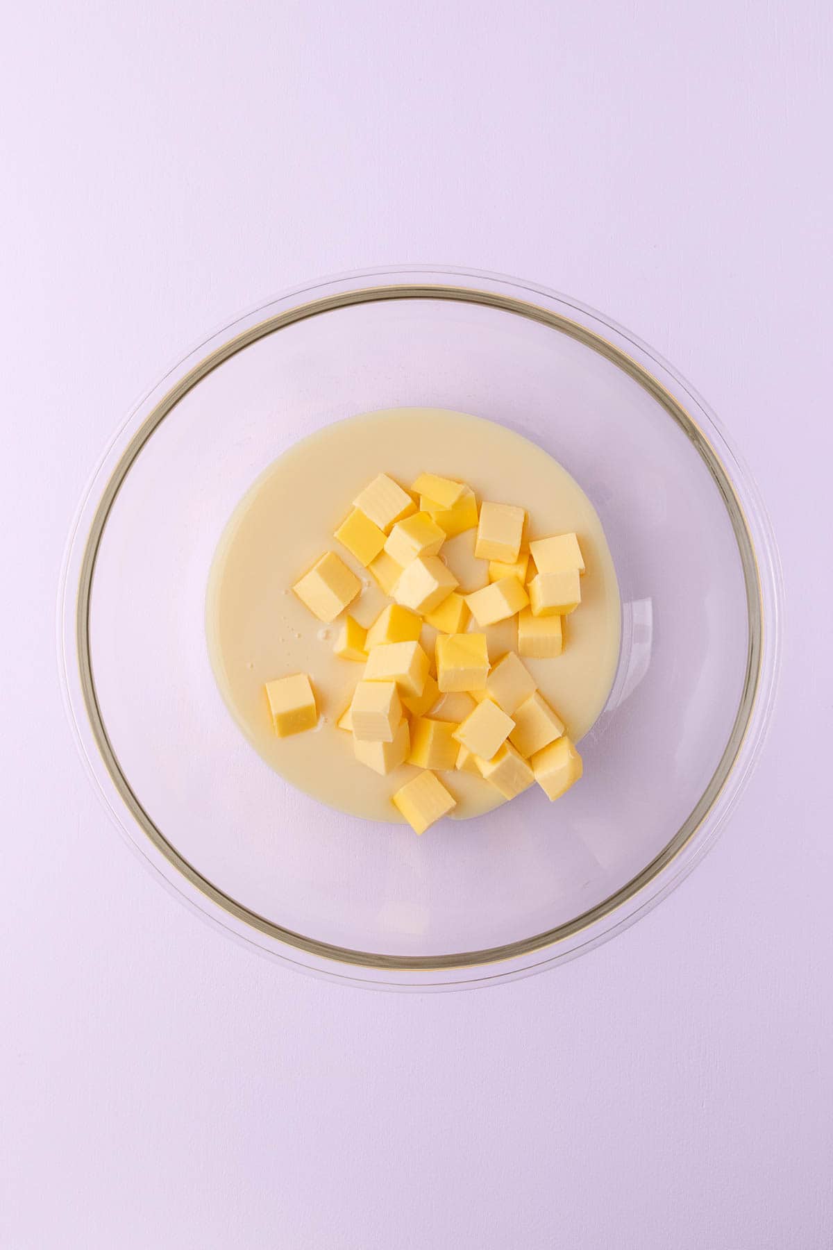 Sweetened condensed milk and chopped butter in a large glass bowl.
