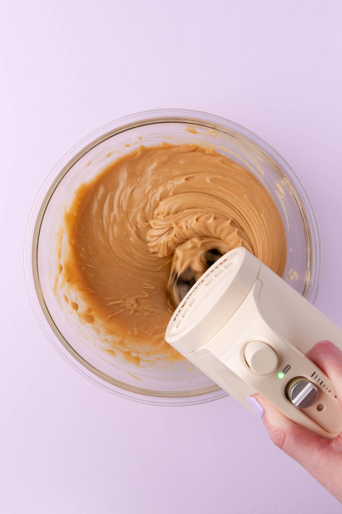The melted caramilk mixture being beaten with a handheld electric mixer.