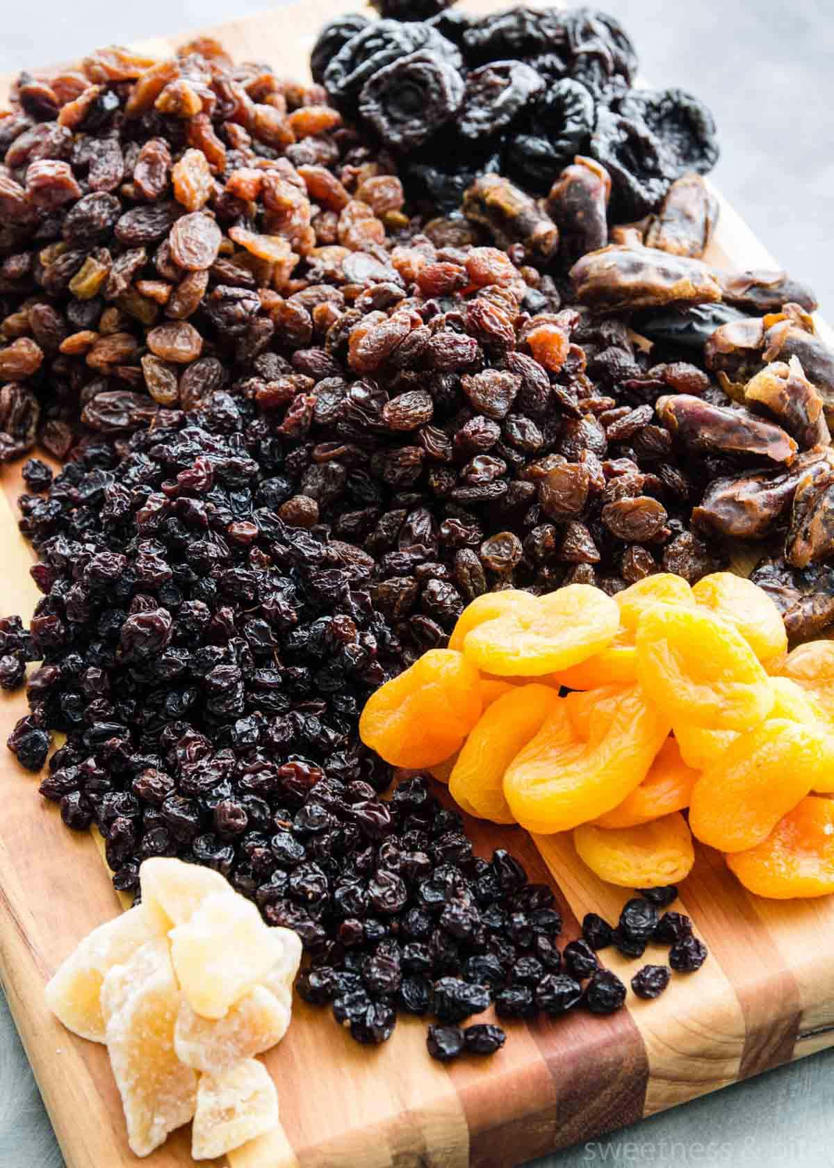 Dried fruits - sultanas, raisins, dates, prunes, currants, apricots and glacé ginger - on a wooden board.
