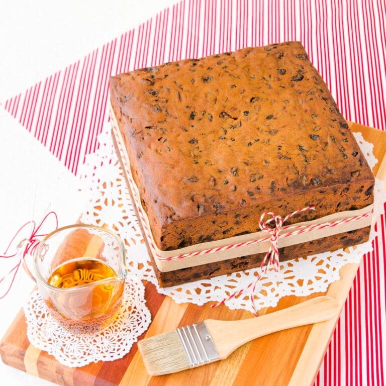 gluten free fruit cake on a wooden board, with a small glass jug of brandy and a pastry brush.
