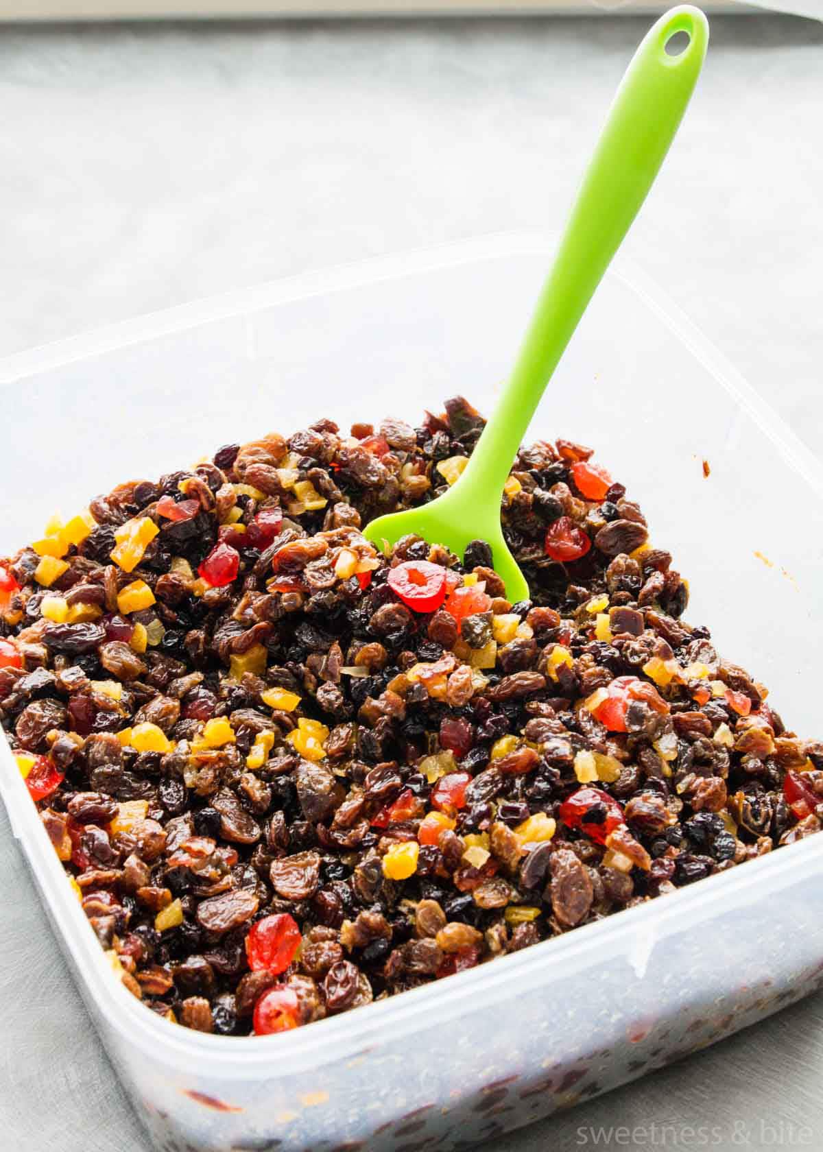 A large square plastic container of mixed dried fruits after soaking in brandy.