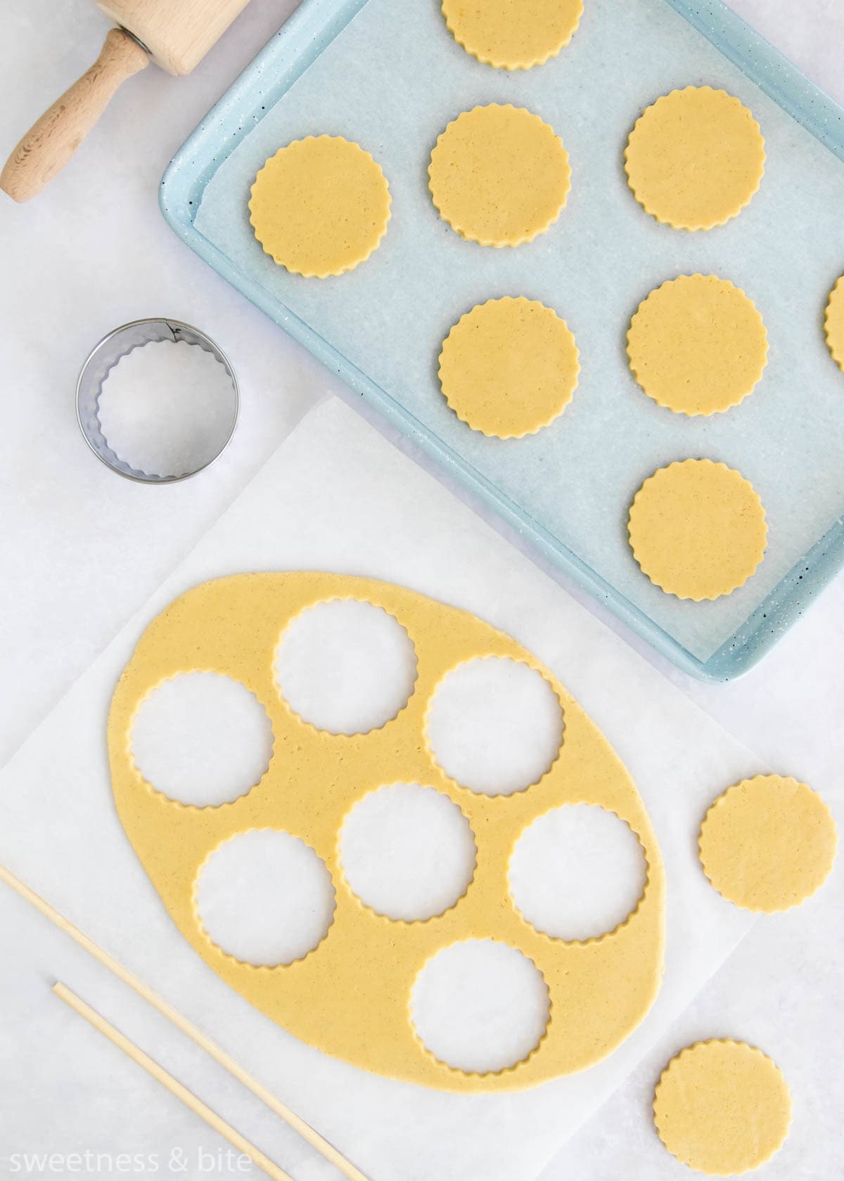 Rolled out cookie dough with scalloped circle shaped cookies cut out.