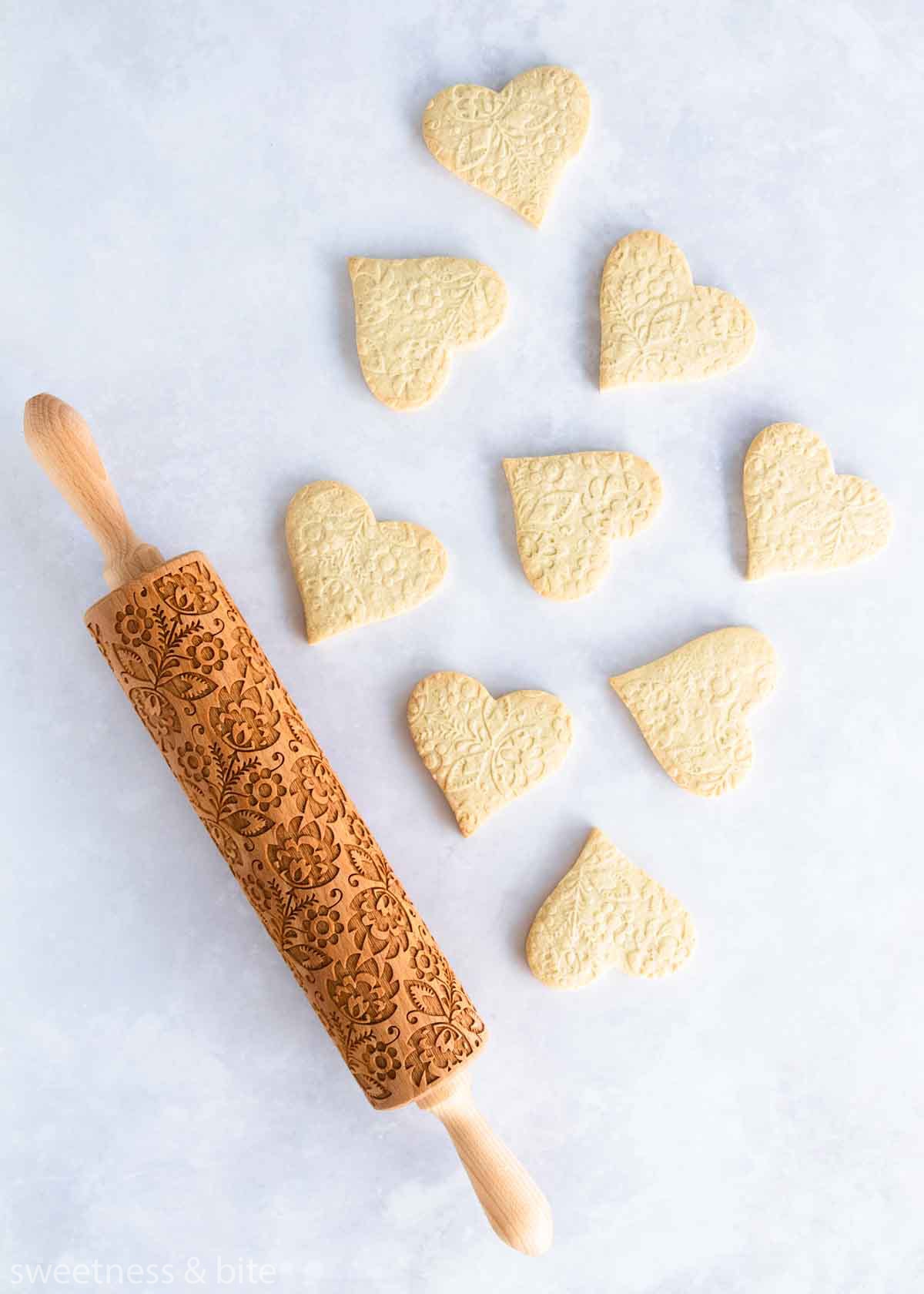 Heart shaped cookies embossed with a floral pattern, with the embossing rolling pin.