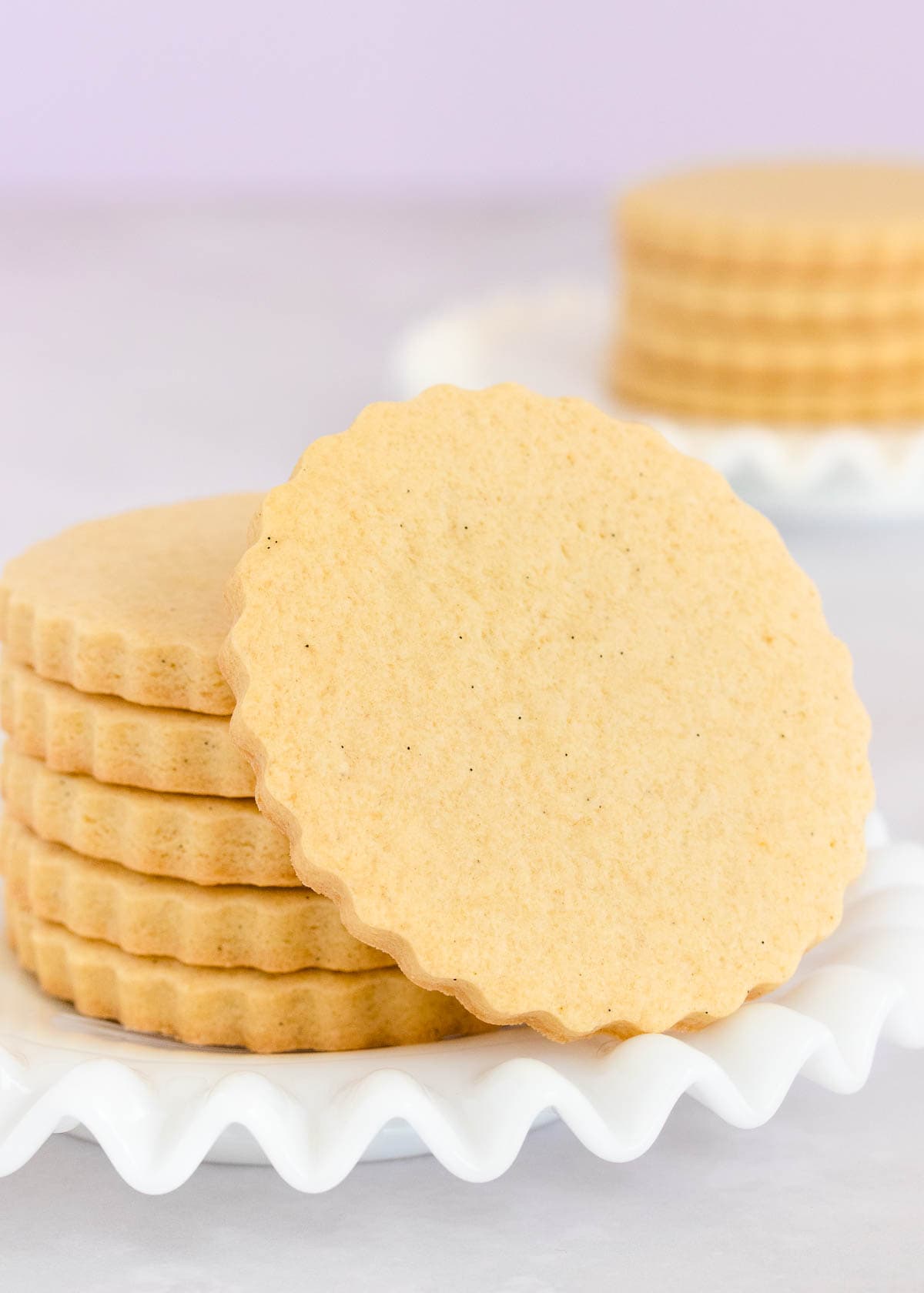 A stack of gluten free sugar cookies on a white glass plate with a ruffled edge. 