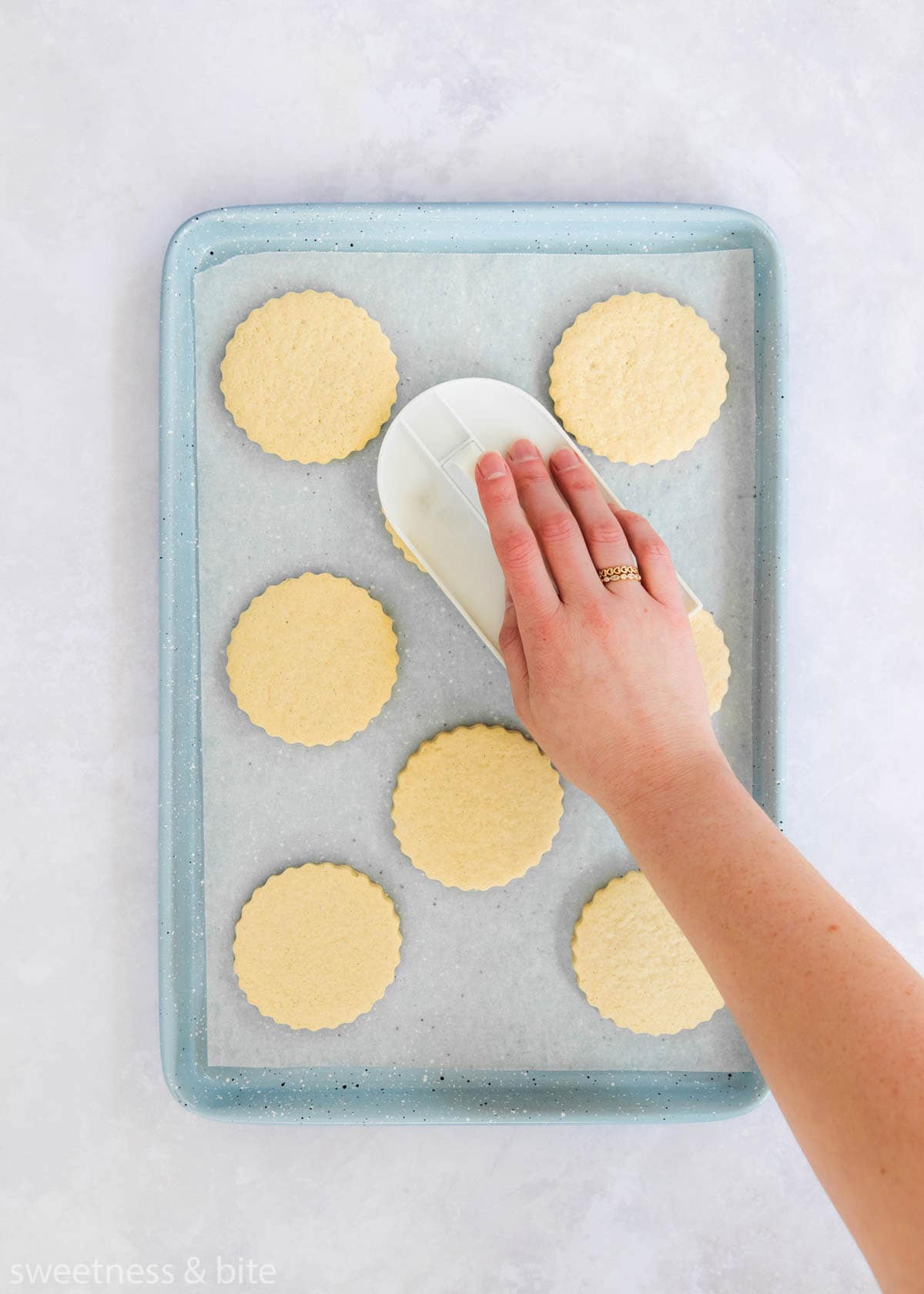 A hand using a white fondant smoother to press down on the tops of the cookies. 