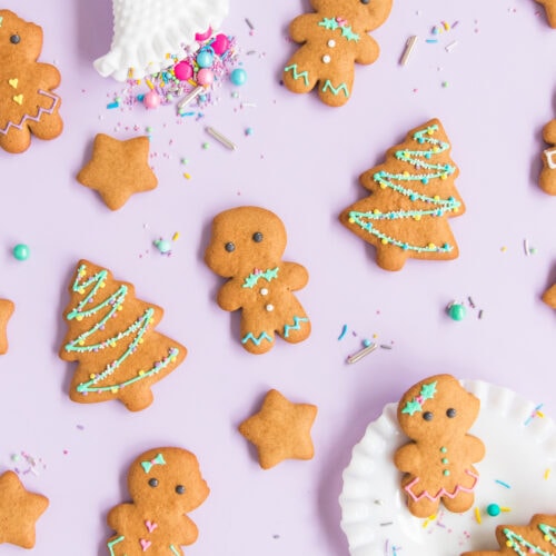 Gluten free gingerbread men and women with gingerbread Christmas tree and star cookies on a purple background, surrounded by pastel and metallic sprinkles.