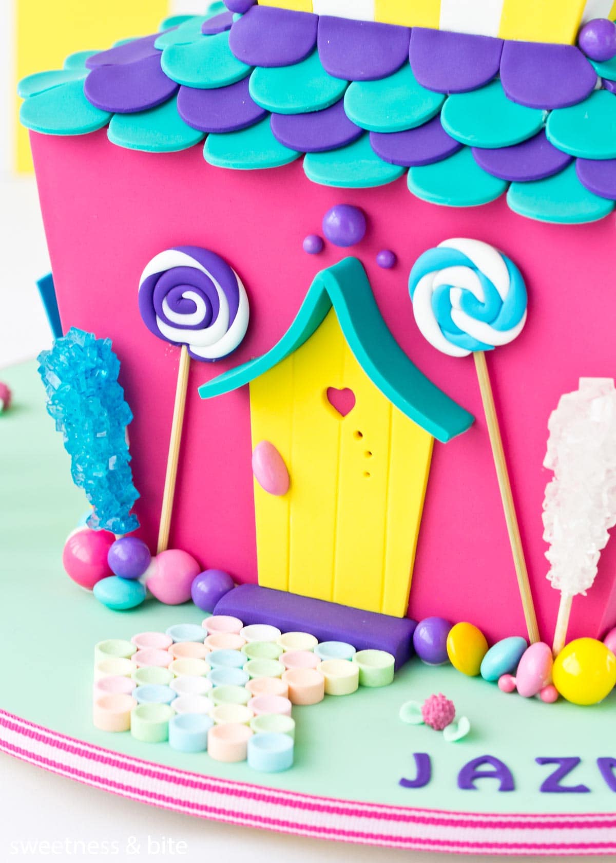 Close up of a candy house cake with a border of assorted lollies attached with royal icing around the bottom of the cake