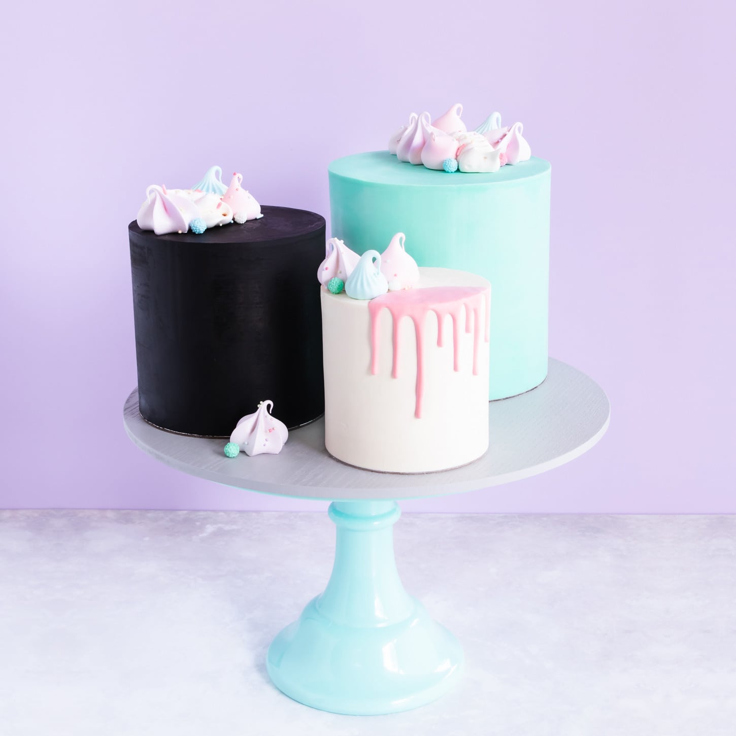 Black, white and teal ganached cakes on a cake stand.