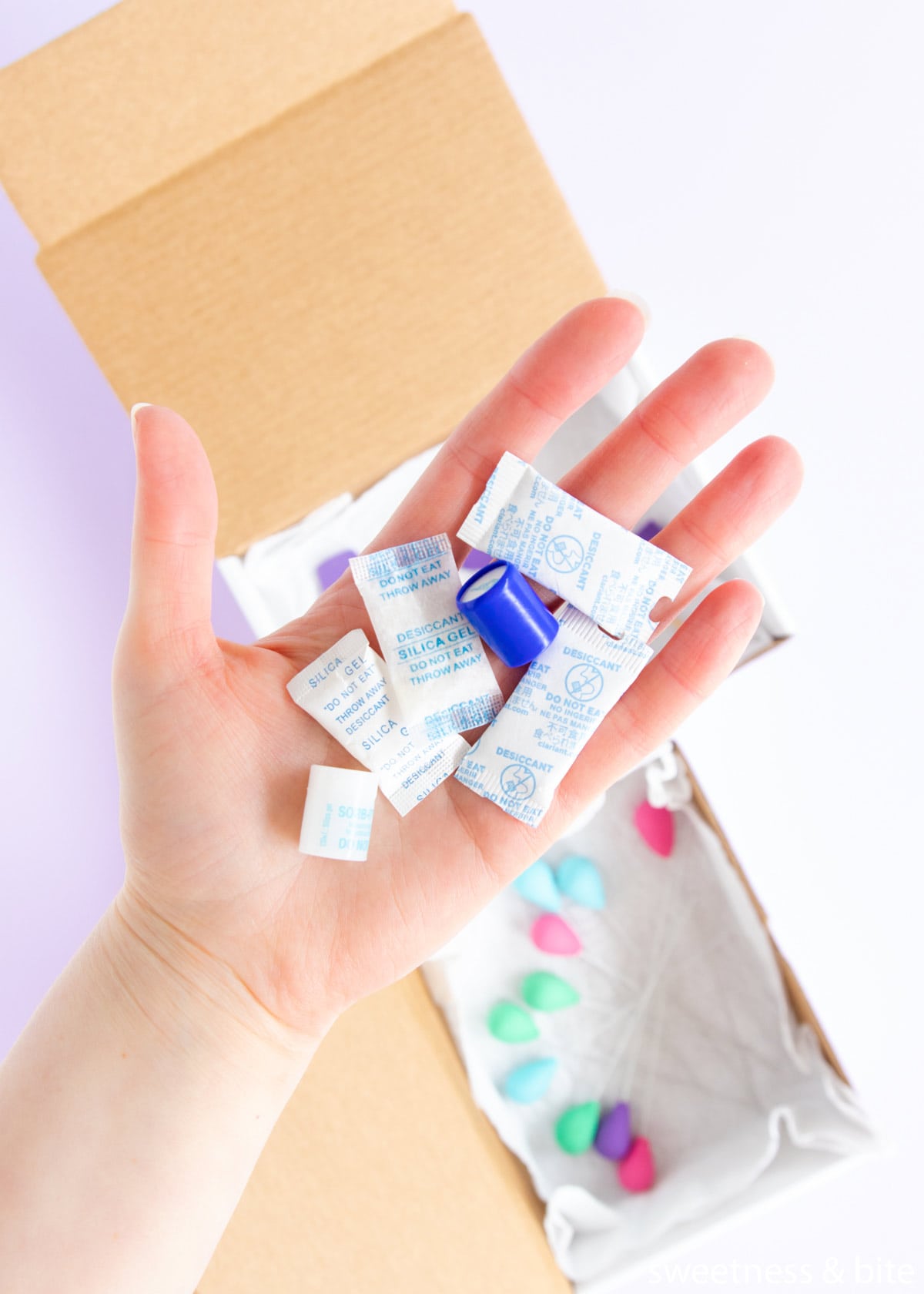 A hand holding silica gel packets to help store dry fondant decorations.