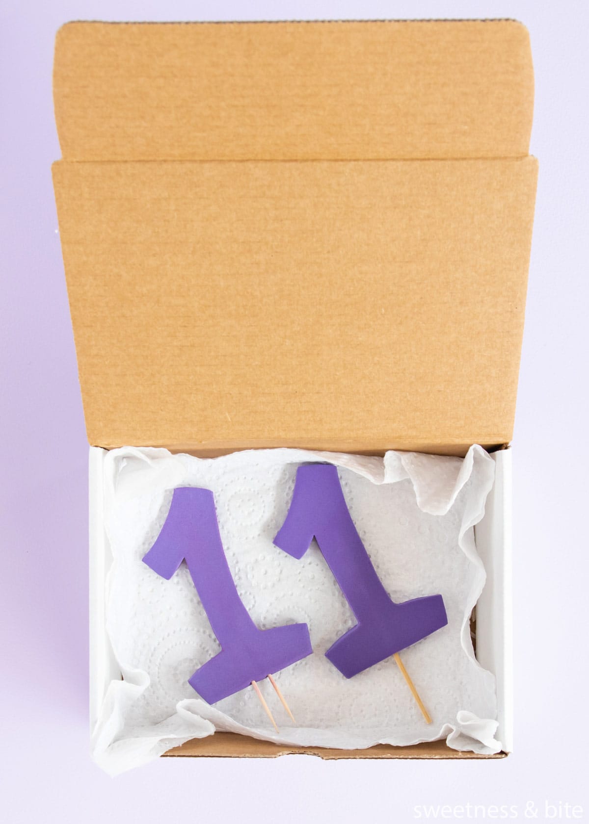 Two purple gumpaste number 1 cake toppers, being stored in a box.