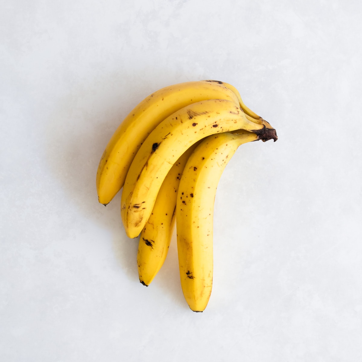 Four ripe bananas on a grey background.