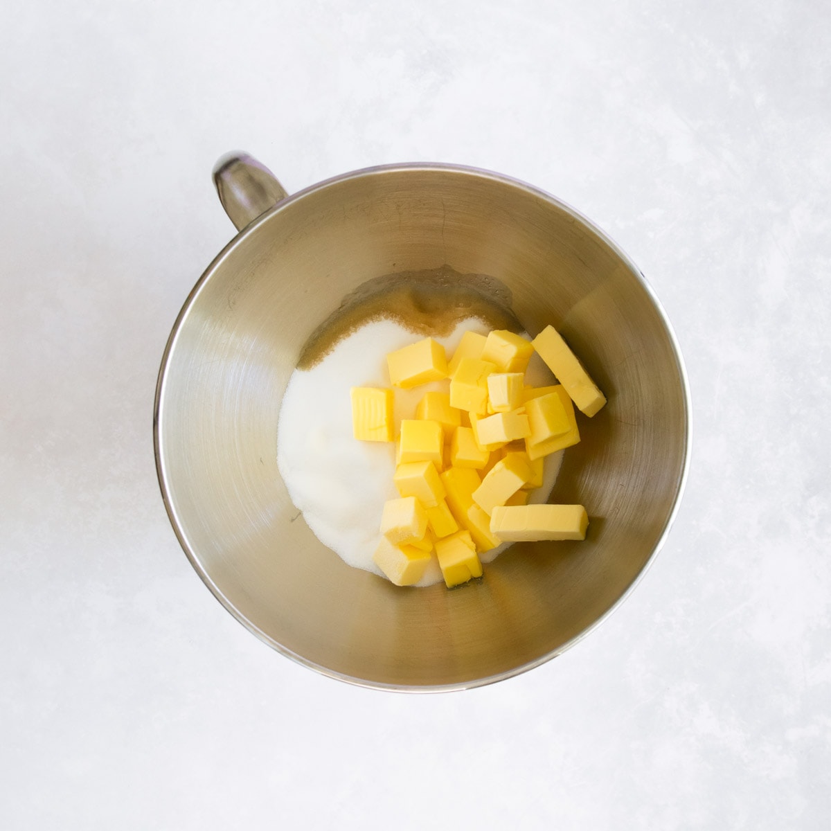 Sugar, butter and vanilla extract in a stainless steel mixer bowl.