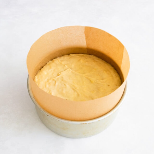 The banana cake batter in a baking tin lined with a tall collar of baking paper.